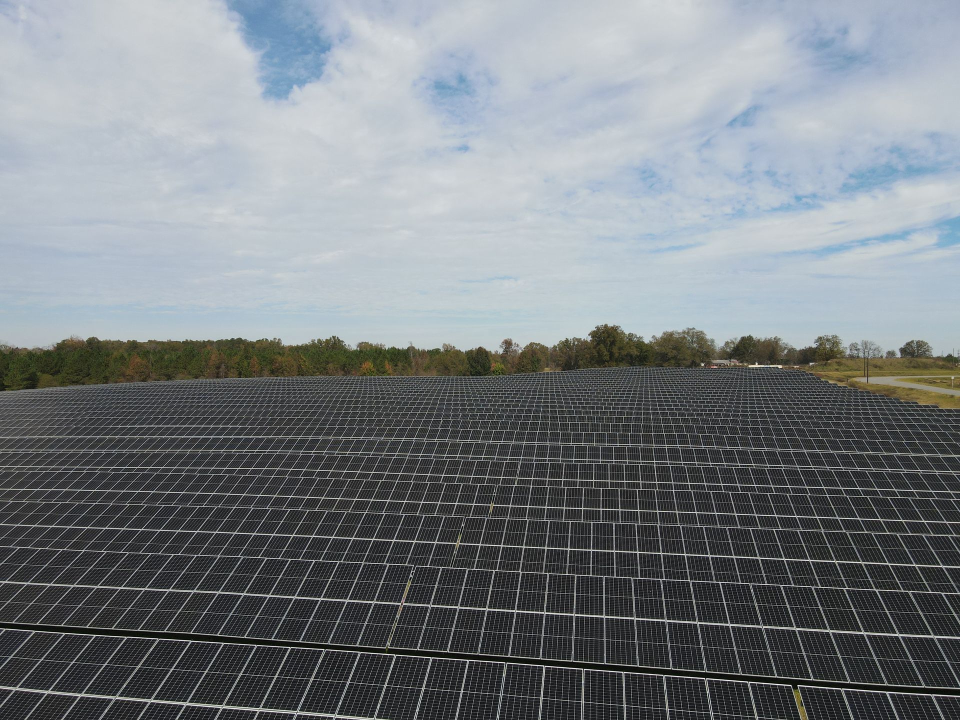 A large field of solar panels against a cloudy sky.