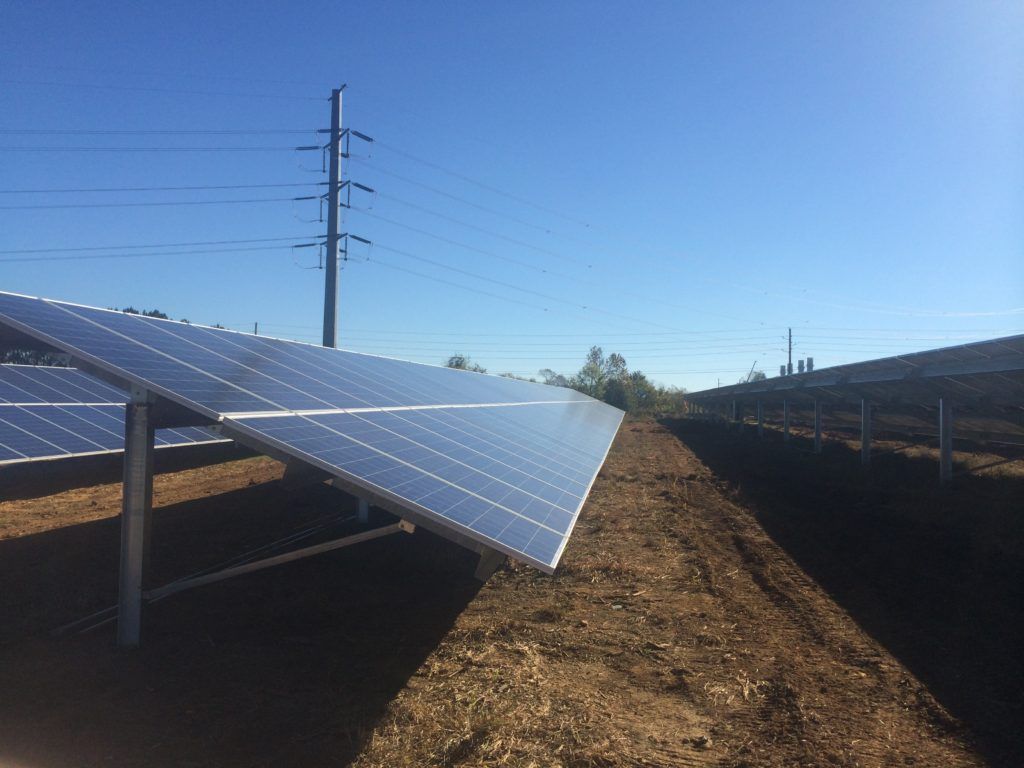 A row of solar panels sitting on top of a dirt field.