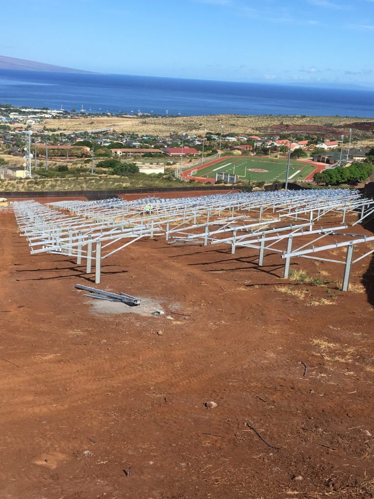 A row of solar panels are sitting on top of a dirt hill overlooking the ocean.