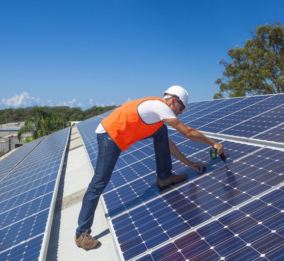 A Man Is Sitting On Top Of A Solar Panel Using A Laptop — Evolution Solar Kingaroy in Kingaroy, QLD