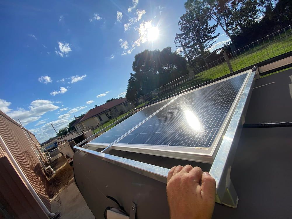 A Person Is Reaching For A Solar Panel On A Roof — Evolution Solar Kingaroy in Kingaroy, QLD