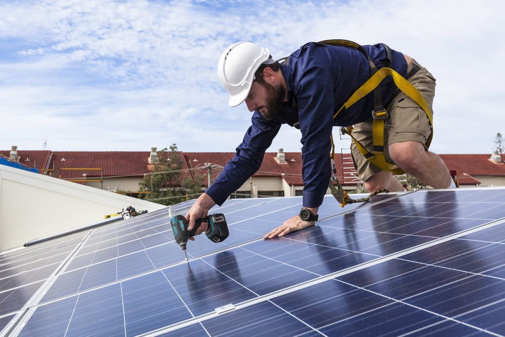 A Man Is Installing Solar Panels On The Roof Of A Building — Evolution Solar Kingaroy in Yarraman, QLD