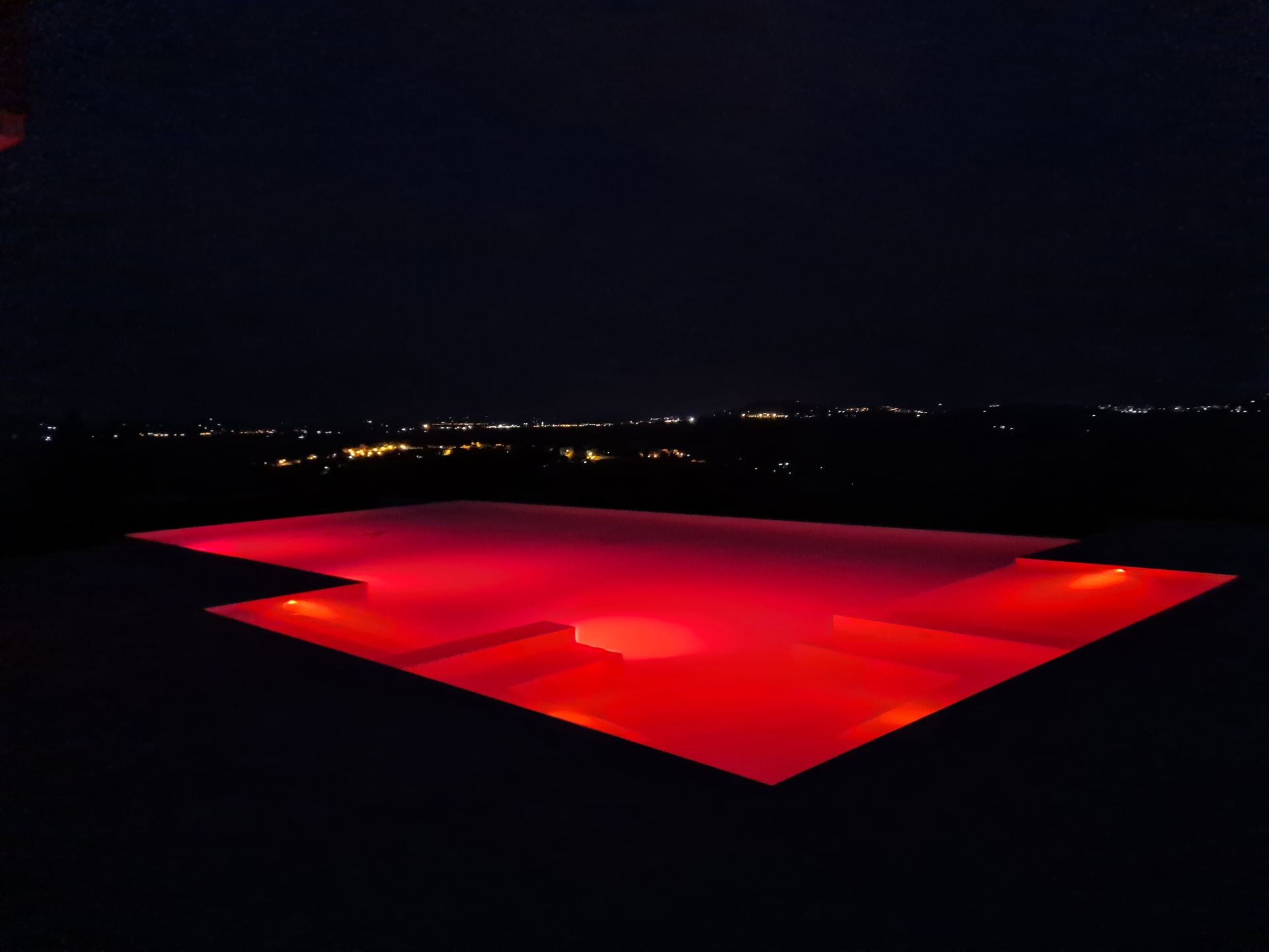Una grande piscina è illuminata di notte con luci rosse