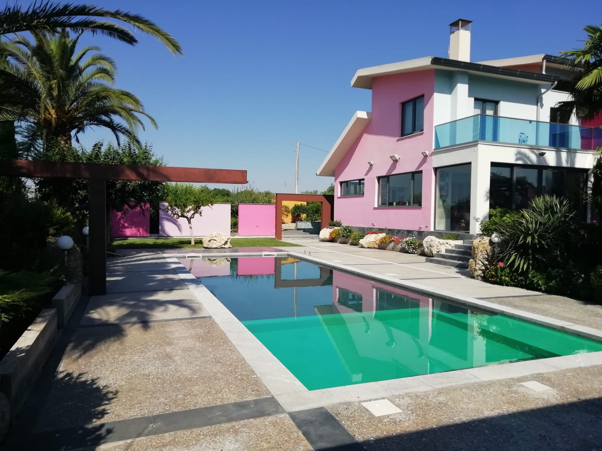 Una casa rosa e bianca con una grande piscina di fronte