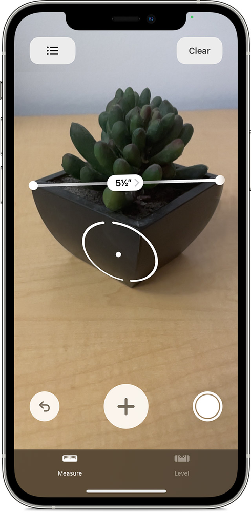 A cell phone is measuring a potted plant on a table.