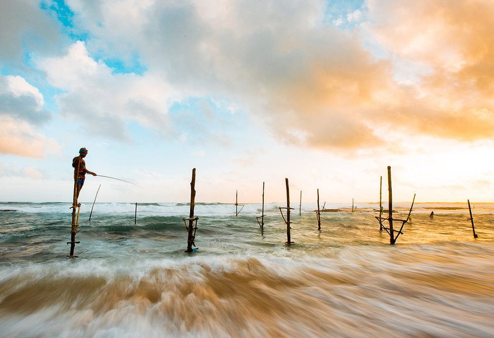 A man is standing on a pole in the ocean fishing.