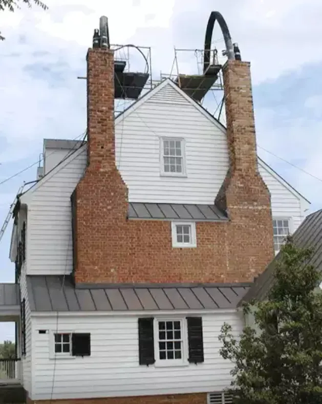 White house with two brick chimneys, scaffolding, and metal roofing.