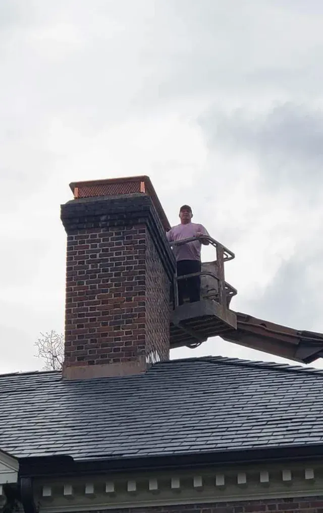 Person on a lift platform near a brick chimney. Cloudy sky above.