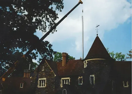 Crane over a stone building with a conical tower and a weathervane, against a cloudy sky.
