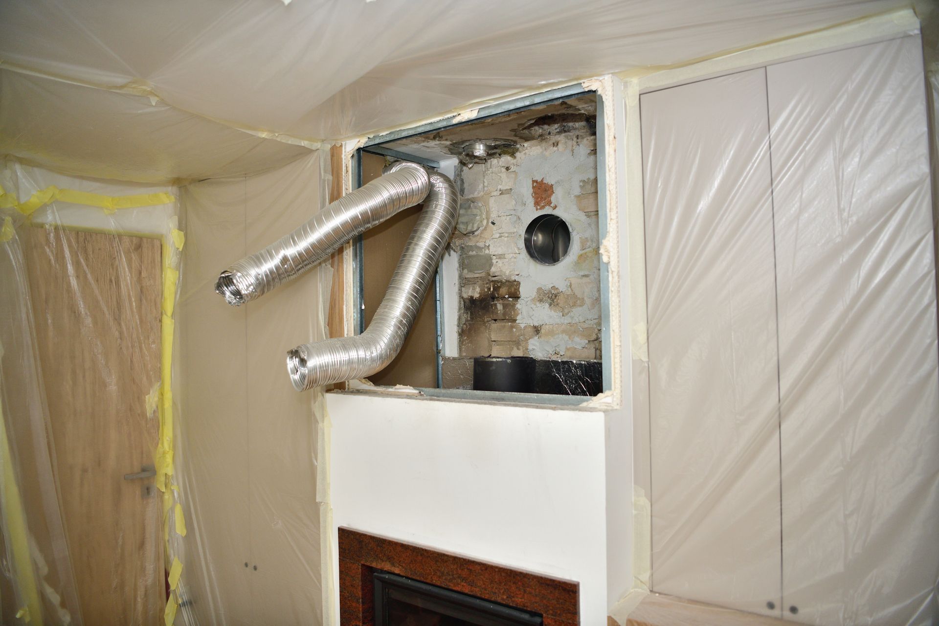 A partially exposed fireplace with flexible ductwork and plastic sheeting covering the walls.