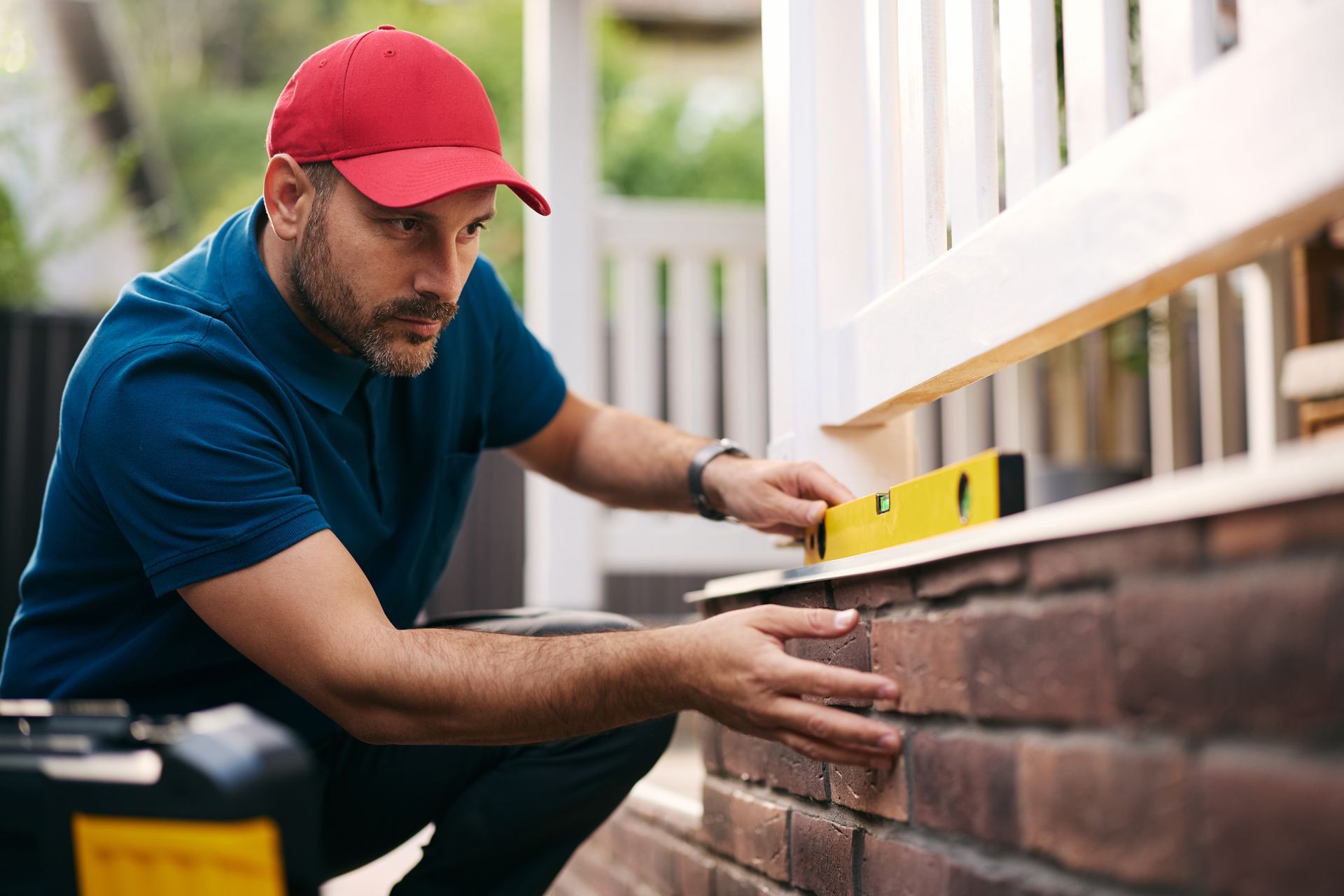 Construction worker on scaffolding, installing a wooden panel on a red brick building. Construction worker laying bricks; yellow hard hat, reflective vest, outdoor setting.