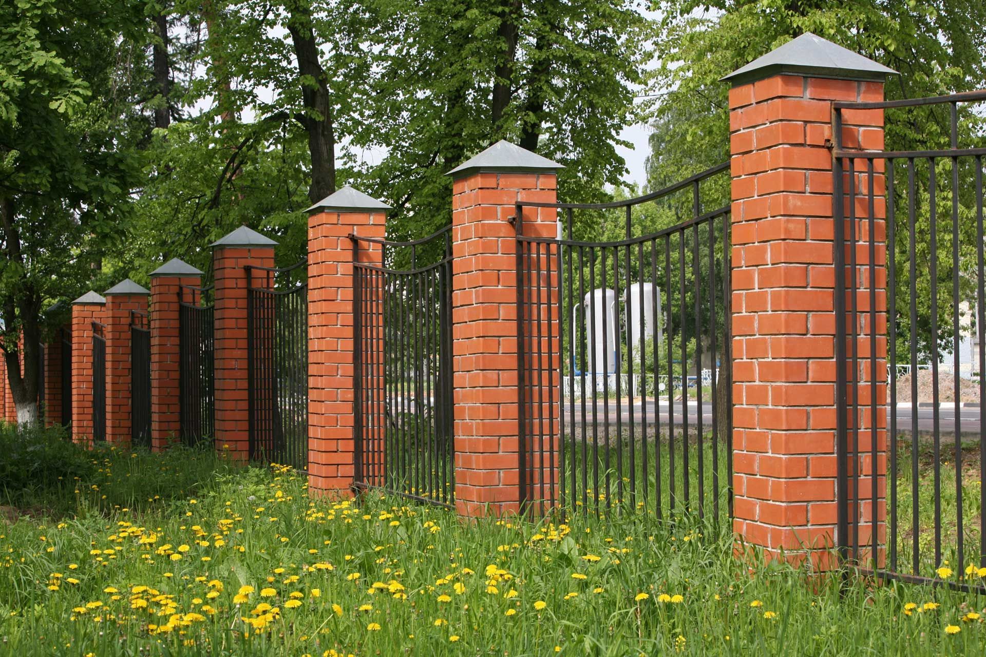 Brick pillars with black metal fence in a grassy area, trees in the background.