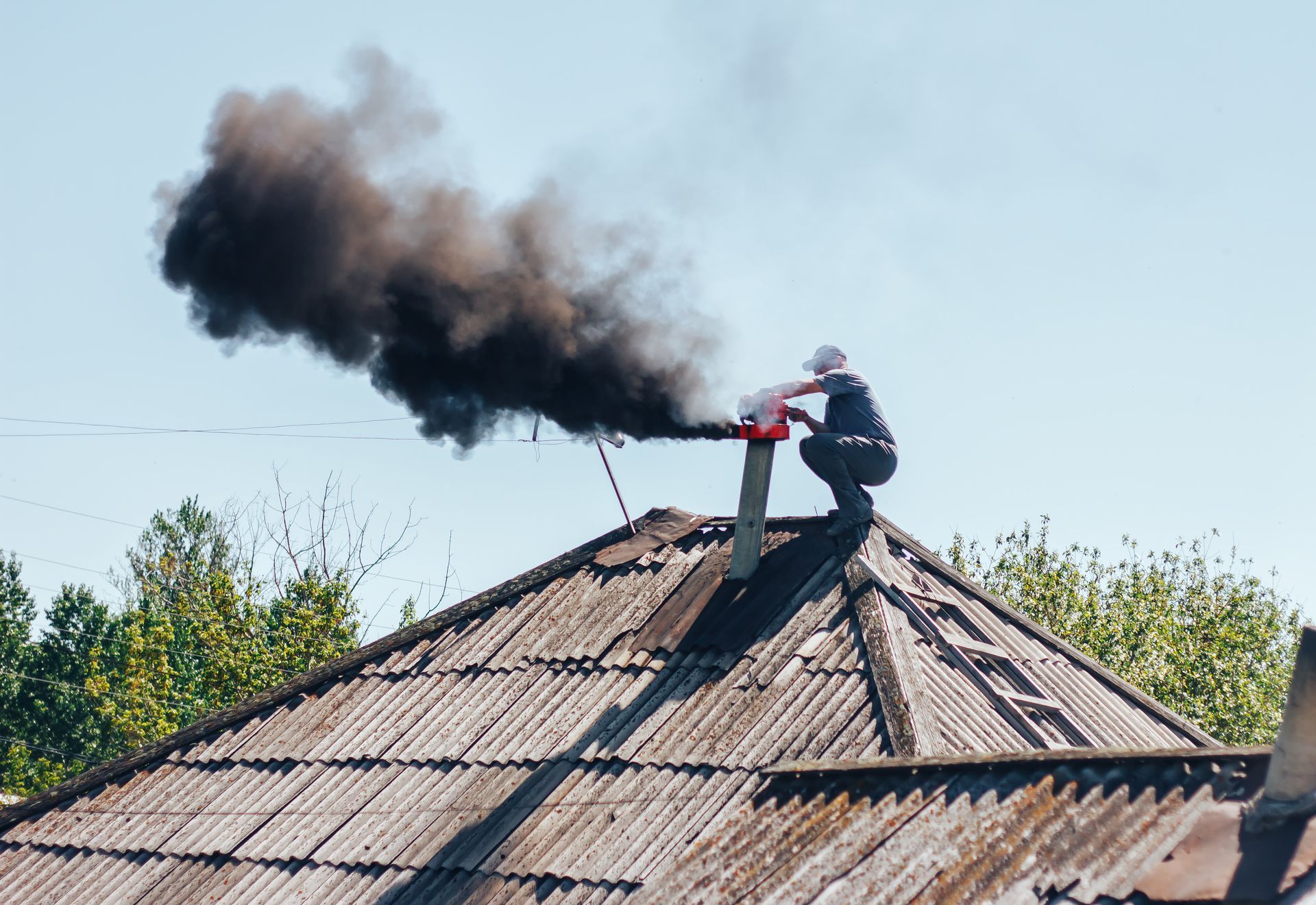 Person on a roof with a chimney spewing black smoke. Person on a roof with a chimney spewing black smoke.