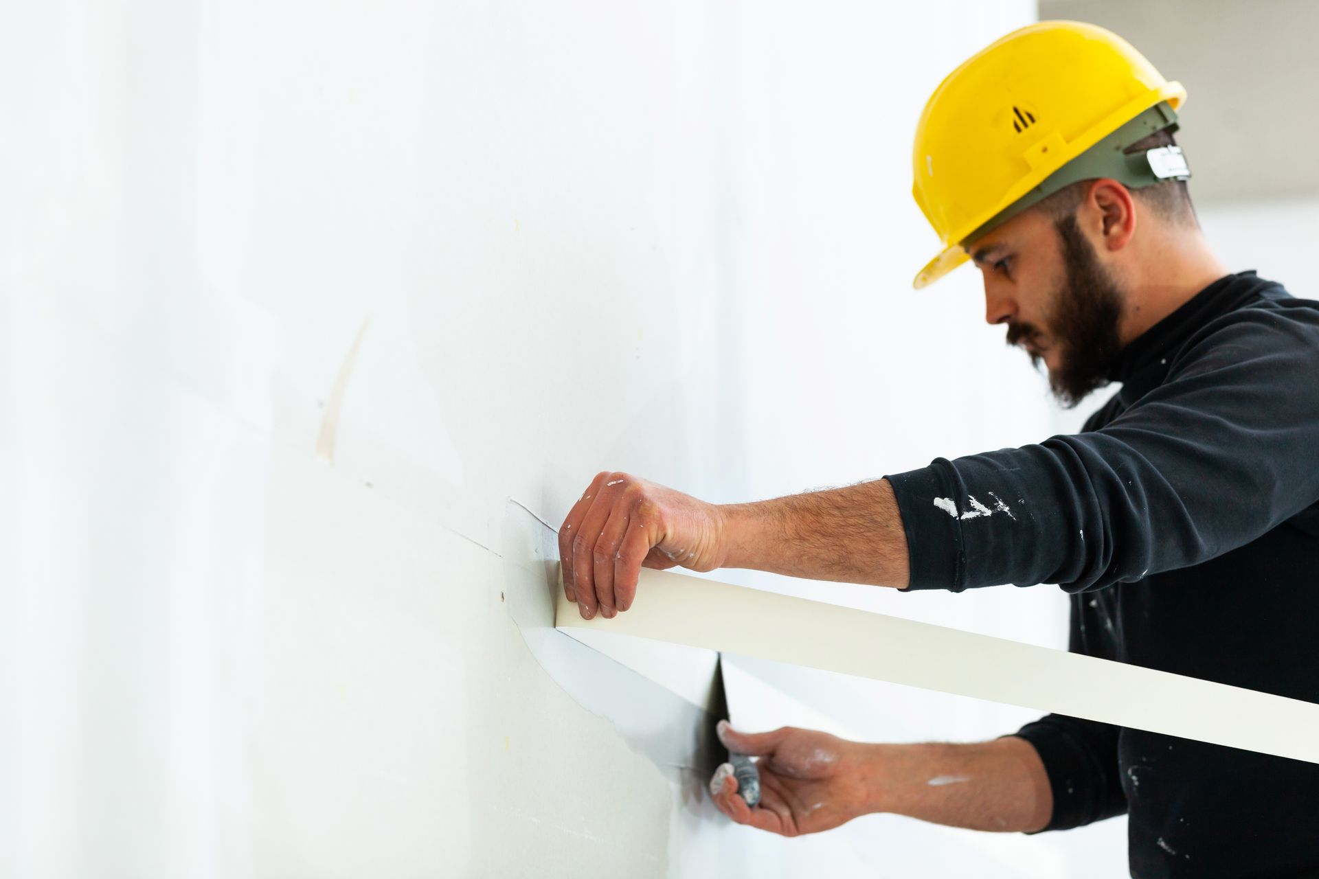 Construction worker applying tape to a wall, wearing a yellow hard hat. Construction worker applying tape to a wall, wearing a yellow hard hat.