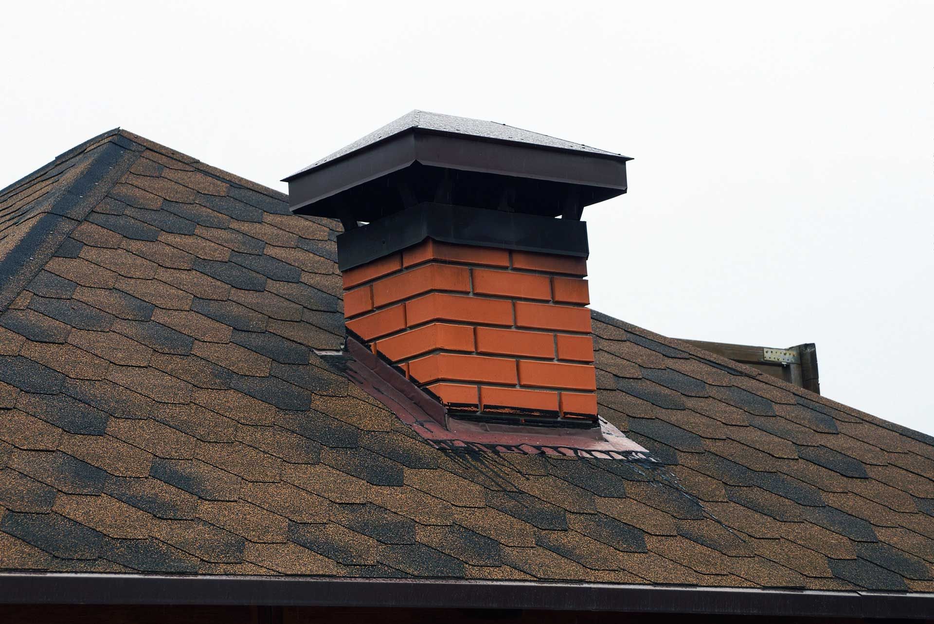 Brick chimney on a brown shingled roof, with a black cap.