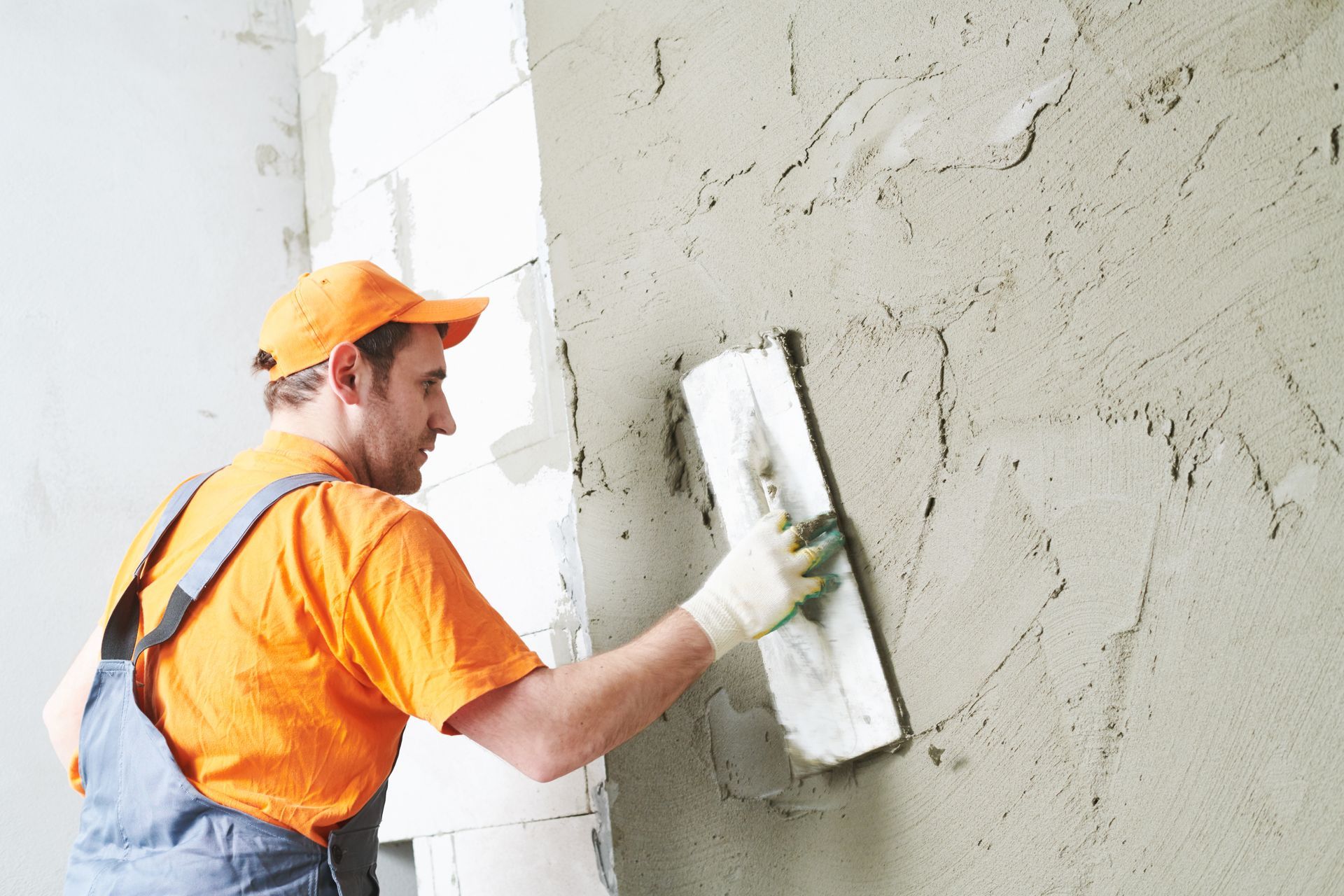Construction worker in orange shirt and overalls applying plaster to a wall with a trowel. Construction worker in orange shirt and overalls applying plaster to a wall with a trowel.