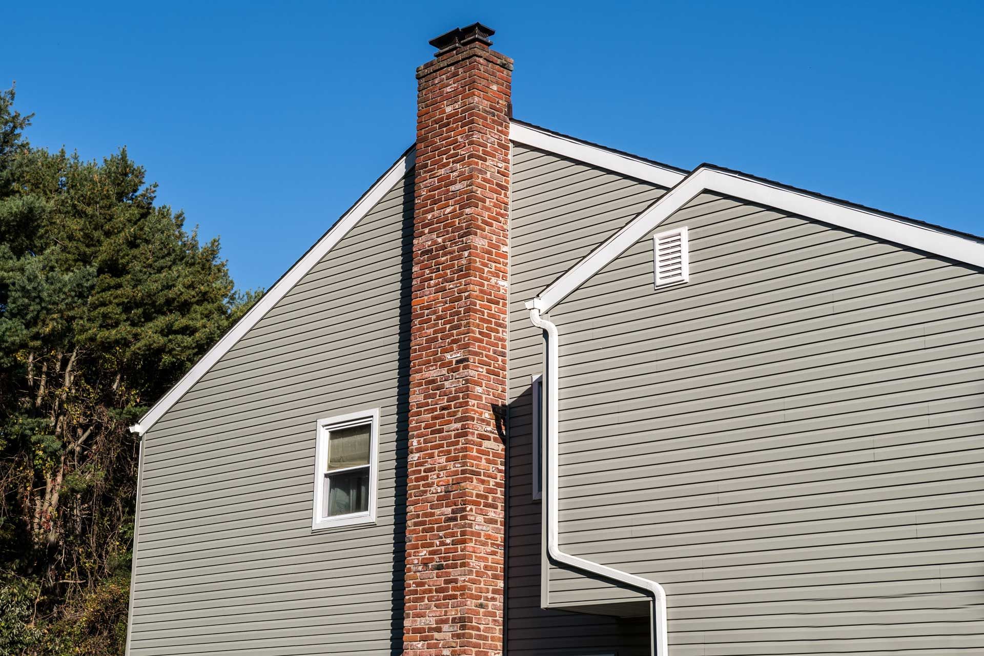 Gray house with a tall brick chimney against a clear blue sky.