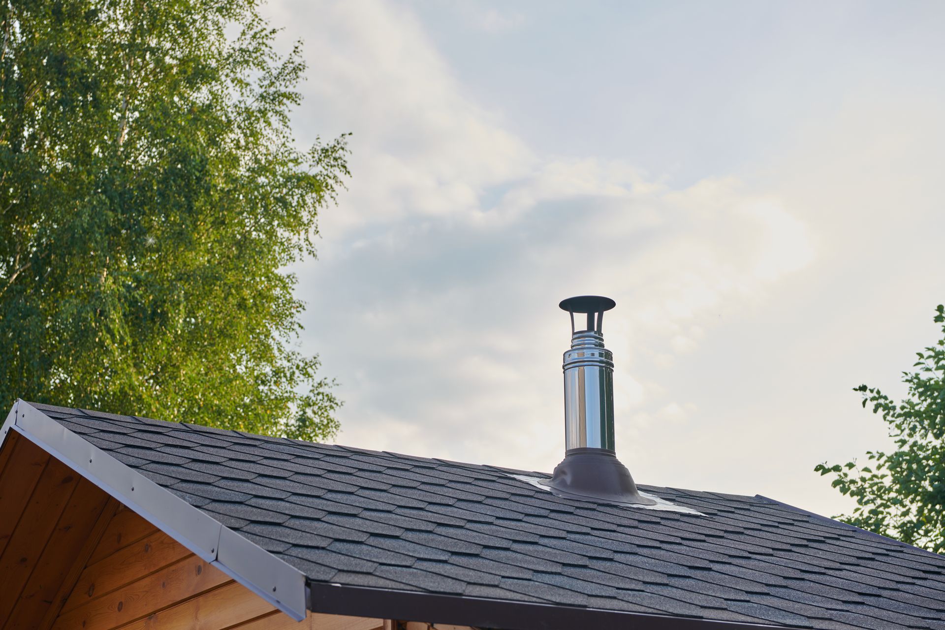 Brown rooftop with a shiny chimney against a partly cloudy sky.