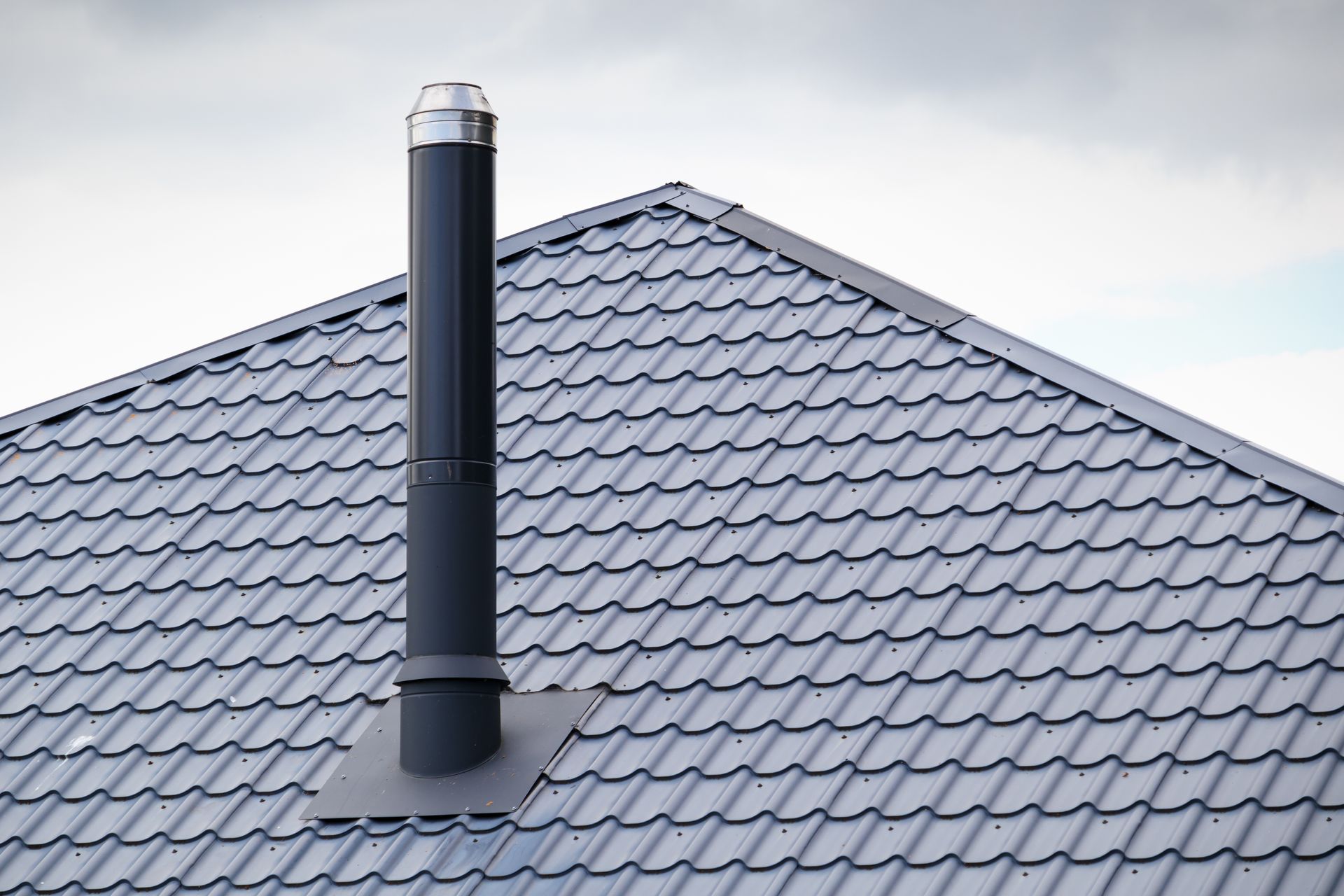 Black chimney on a gray metal roof under an overcast sky. Black chimney on a gray metal roof under an overcast sky.