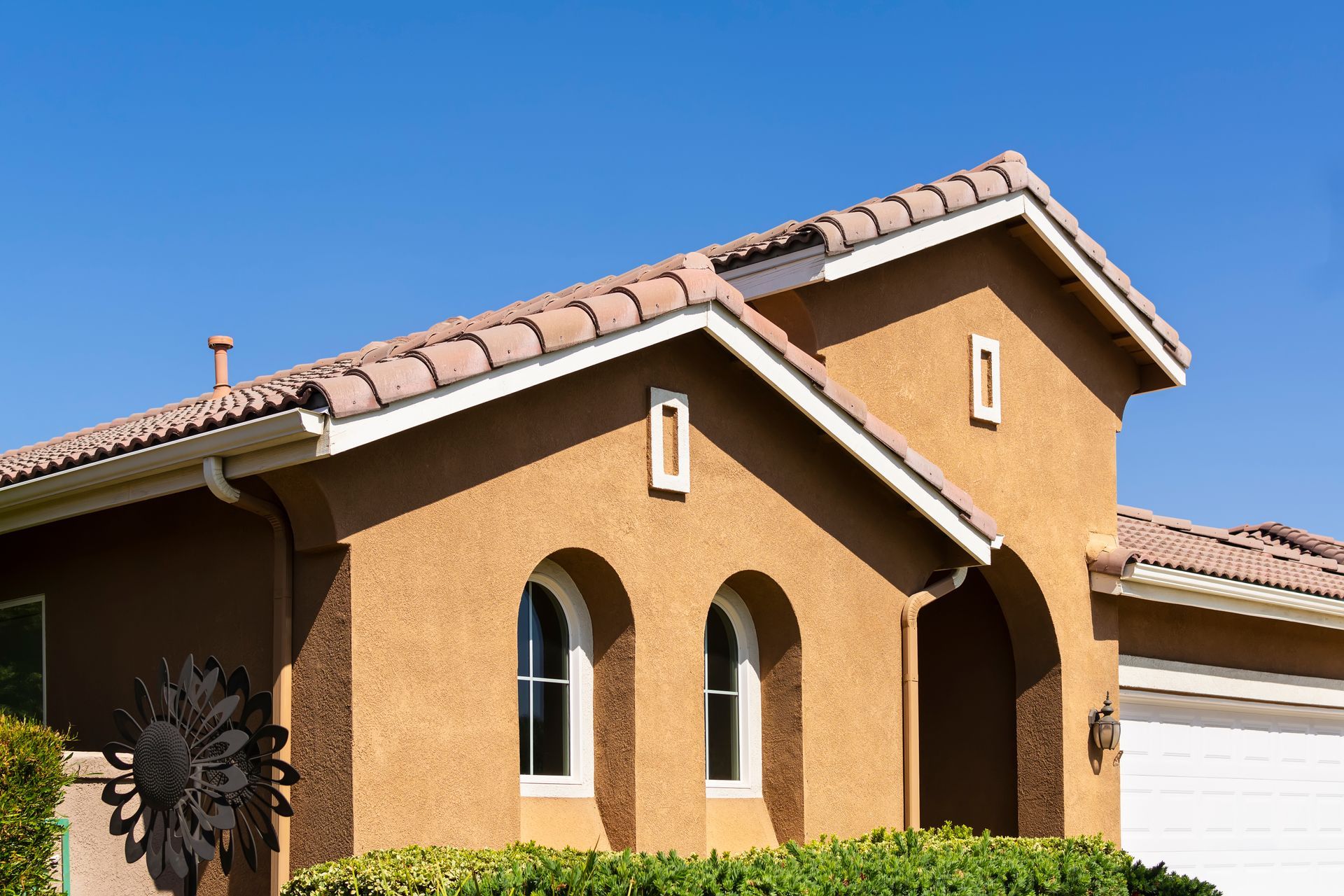 Tan stucco house with a tile roof, arched windows, and bright blue sky. Tan stucco house with a tile roof, arched windows, and bright blue sky.