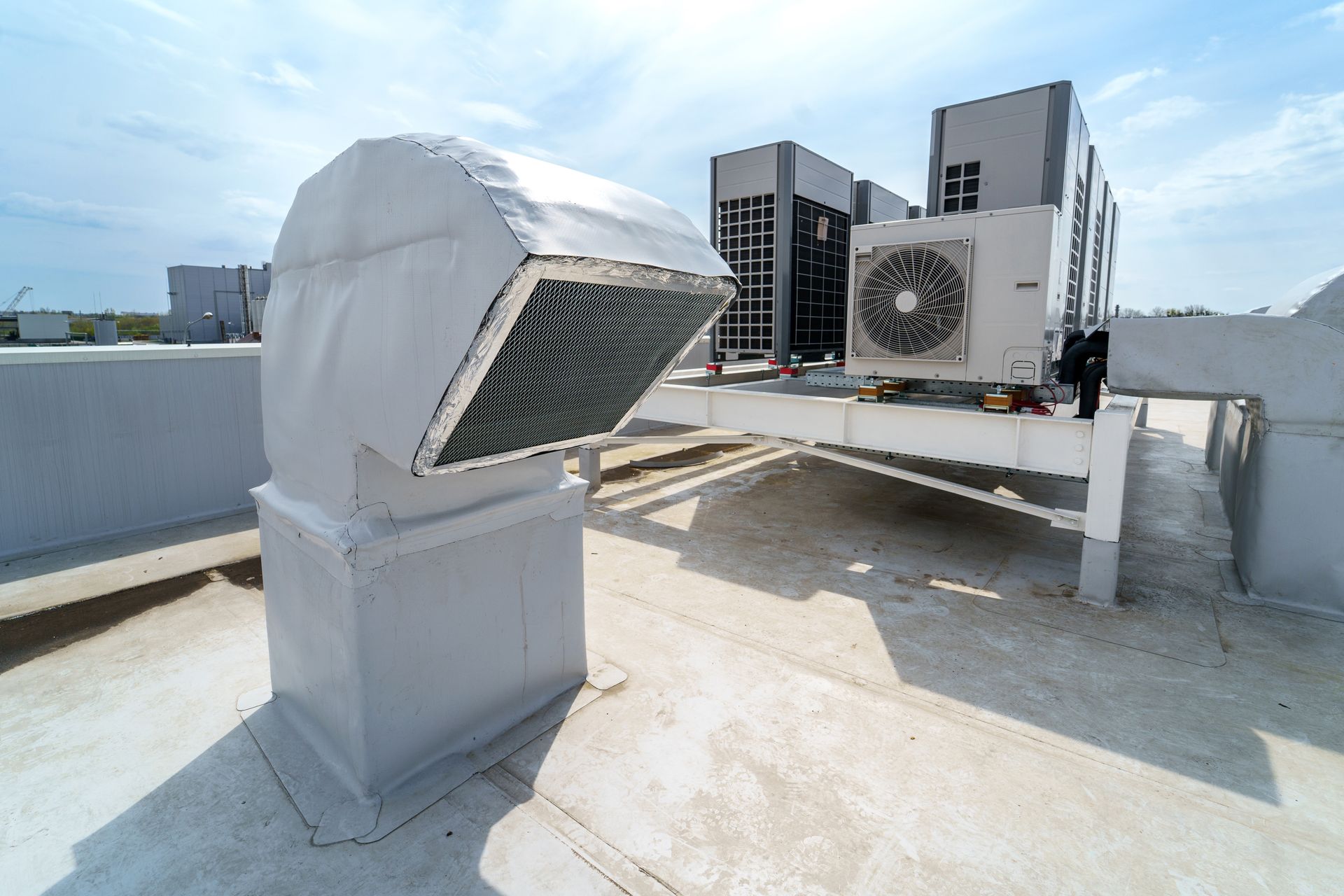 Rooftop ventilation unit and HVAC equipment on a concrete roof under a blue sky.