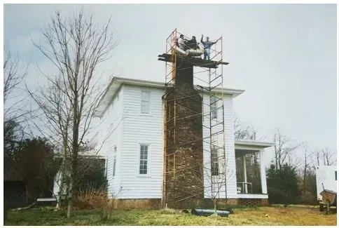 Workers on scaffolding repair chimney of a white house on a cloudy day.