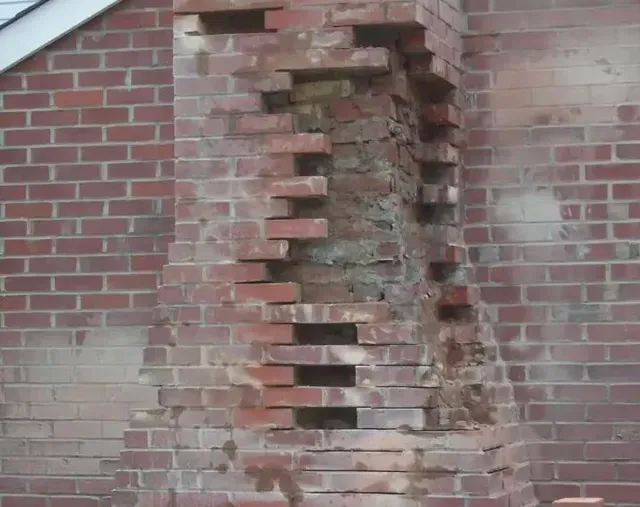 Damaged brick chimney with missing bricks, revealing mortar and interior.