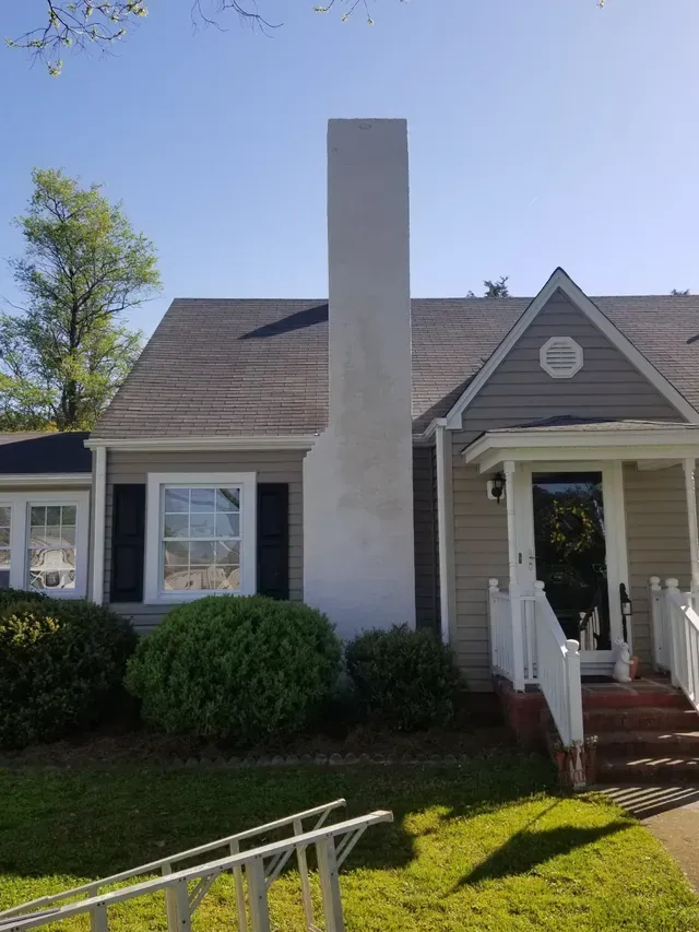 Chimney on a house with a gray roof and siding, next to a window and porch.
