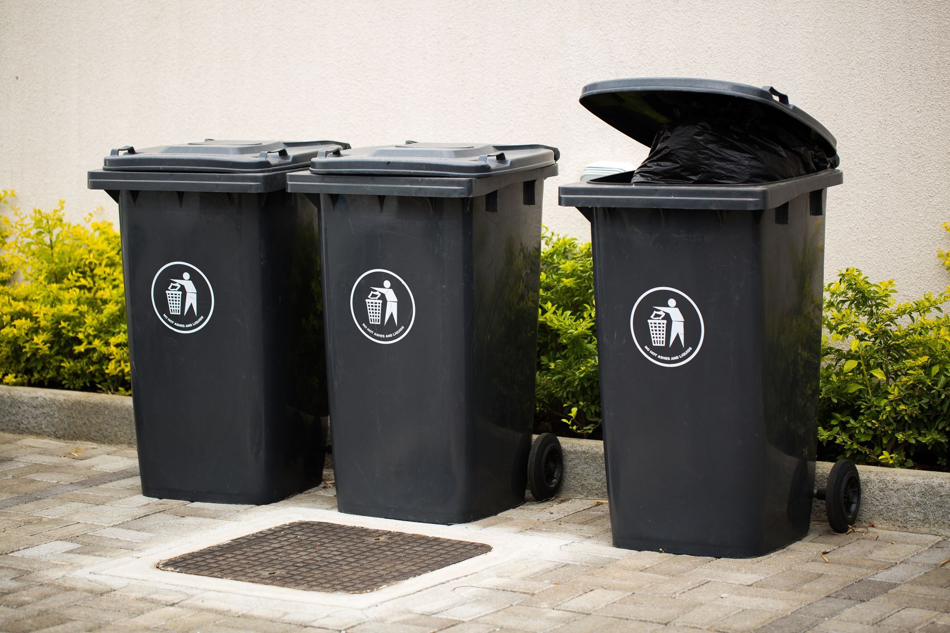 Trois poubelles noires sont posées l'une à côté de l'autre sur un trottoir.