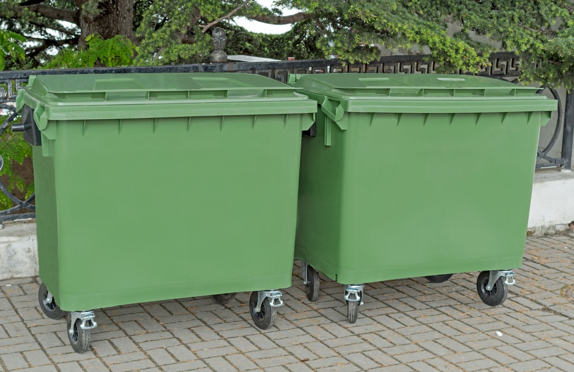 Deux poubelles vertes sont posées l'une à côté de l'autre sur un trottoir en briques.