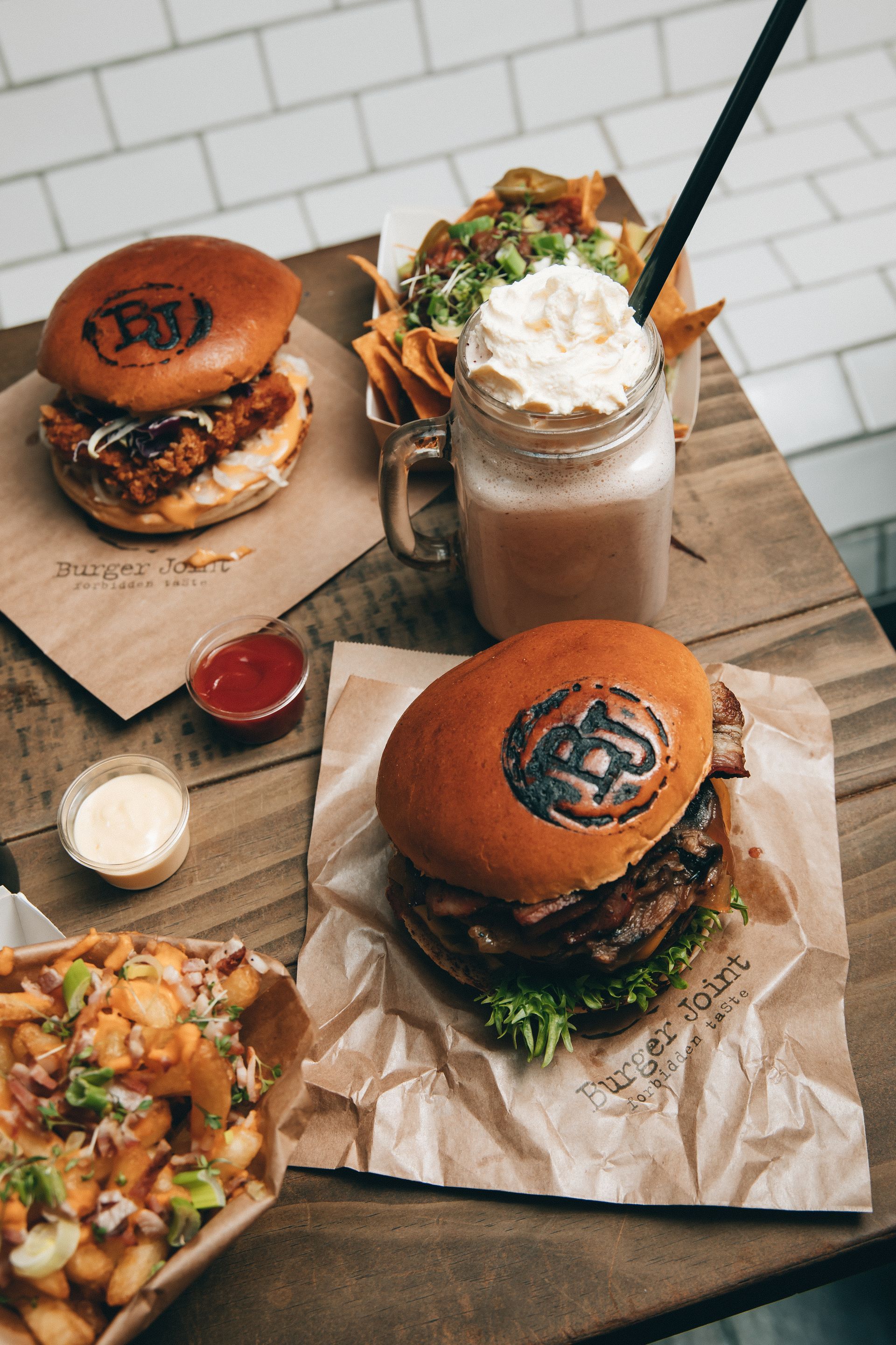 To burgere, pommes frites og en milkshake på et trebord.
