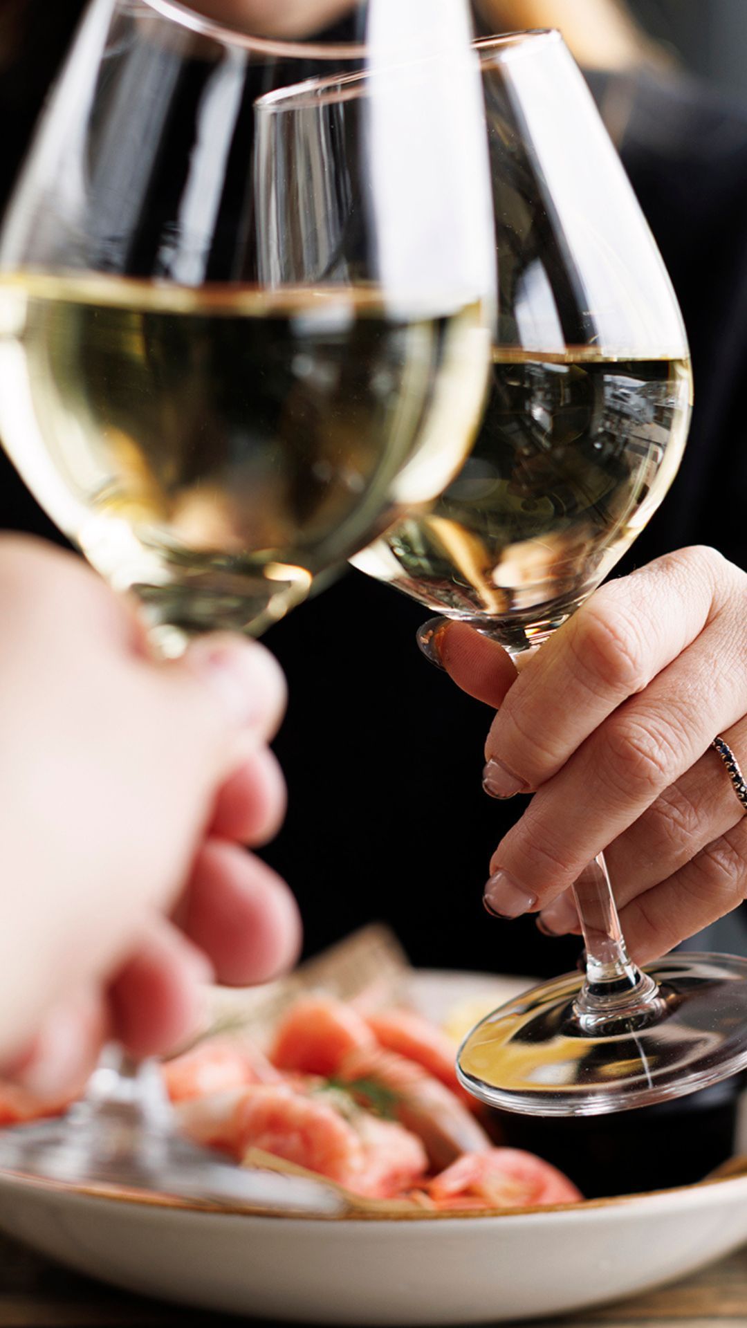 To personer holder vinglass over en tallerken med mat.