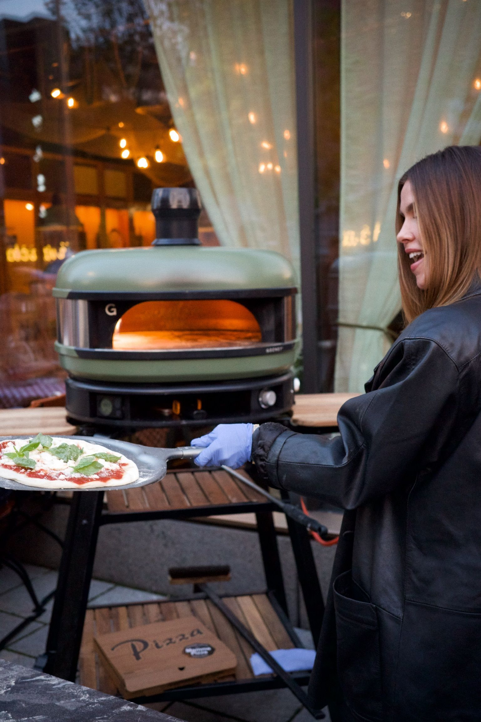 En kvinne lager en pizza i en utendørs ovn.