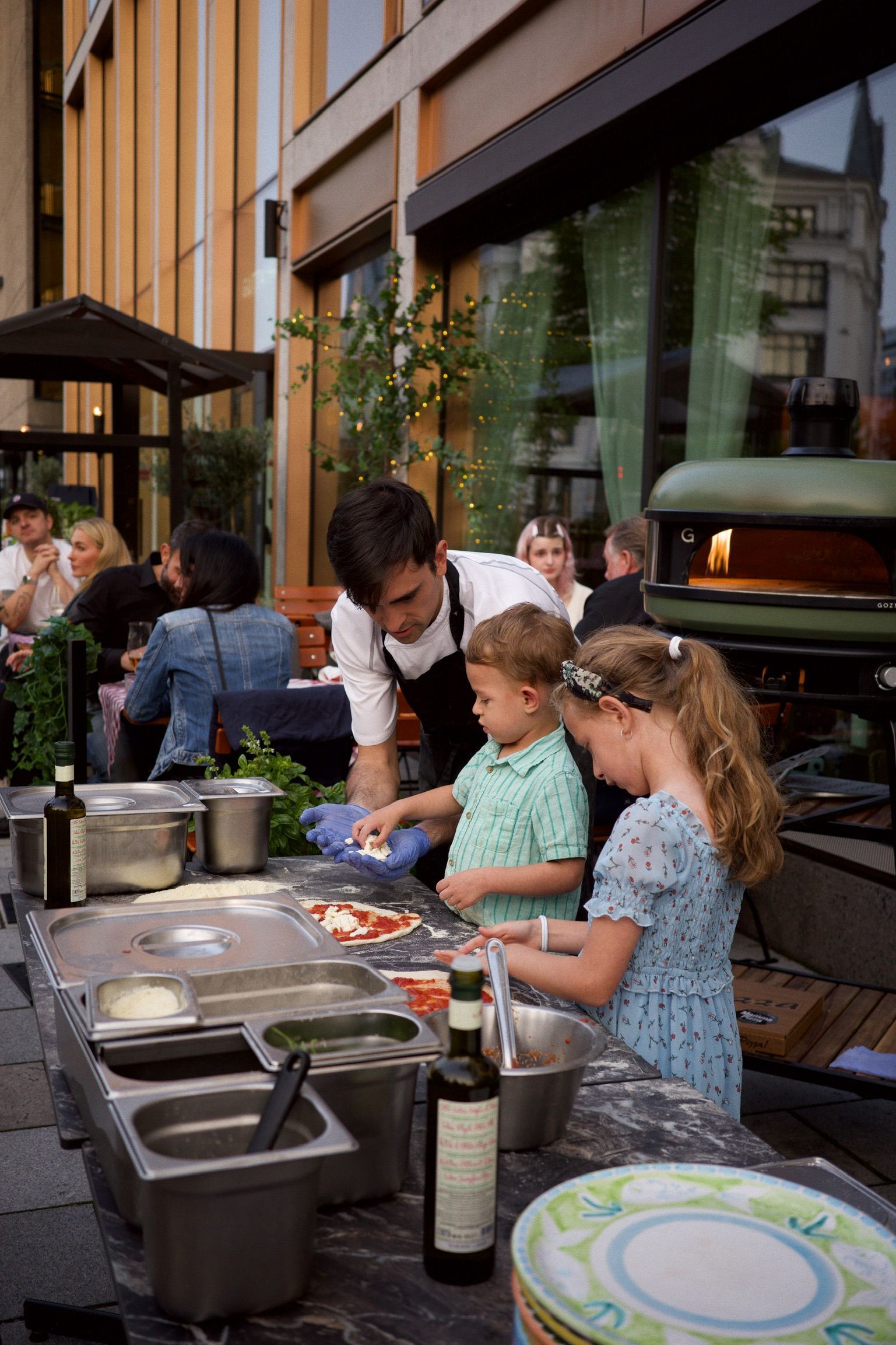 En mann og to barn lager pizza utenfor en restaurant.