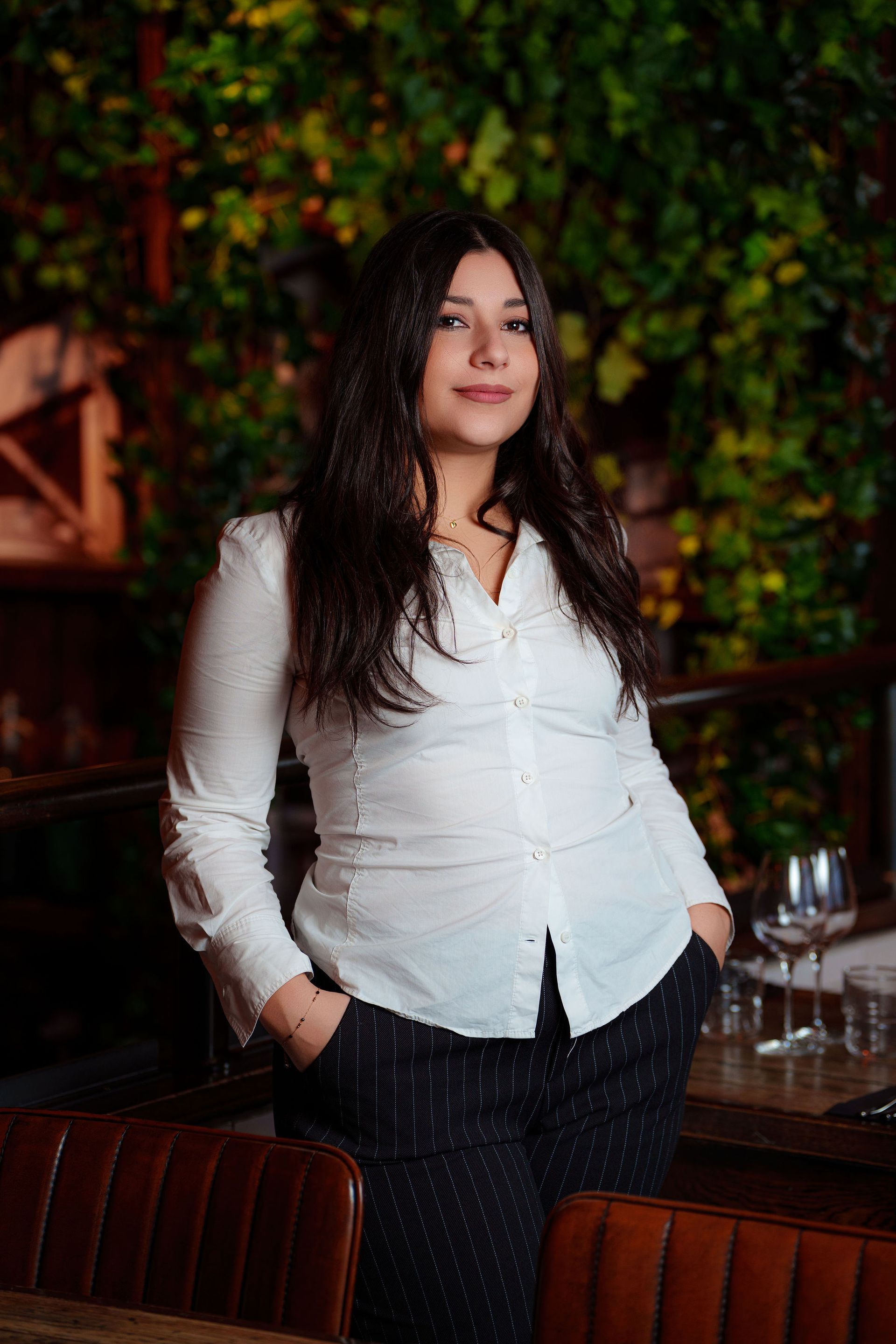 En kvinne i hvit skjorte står foran grønn blader som bakgrunn 