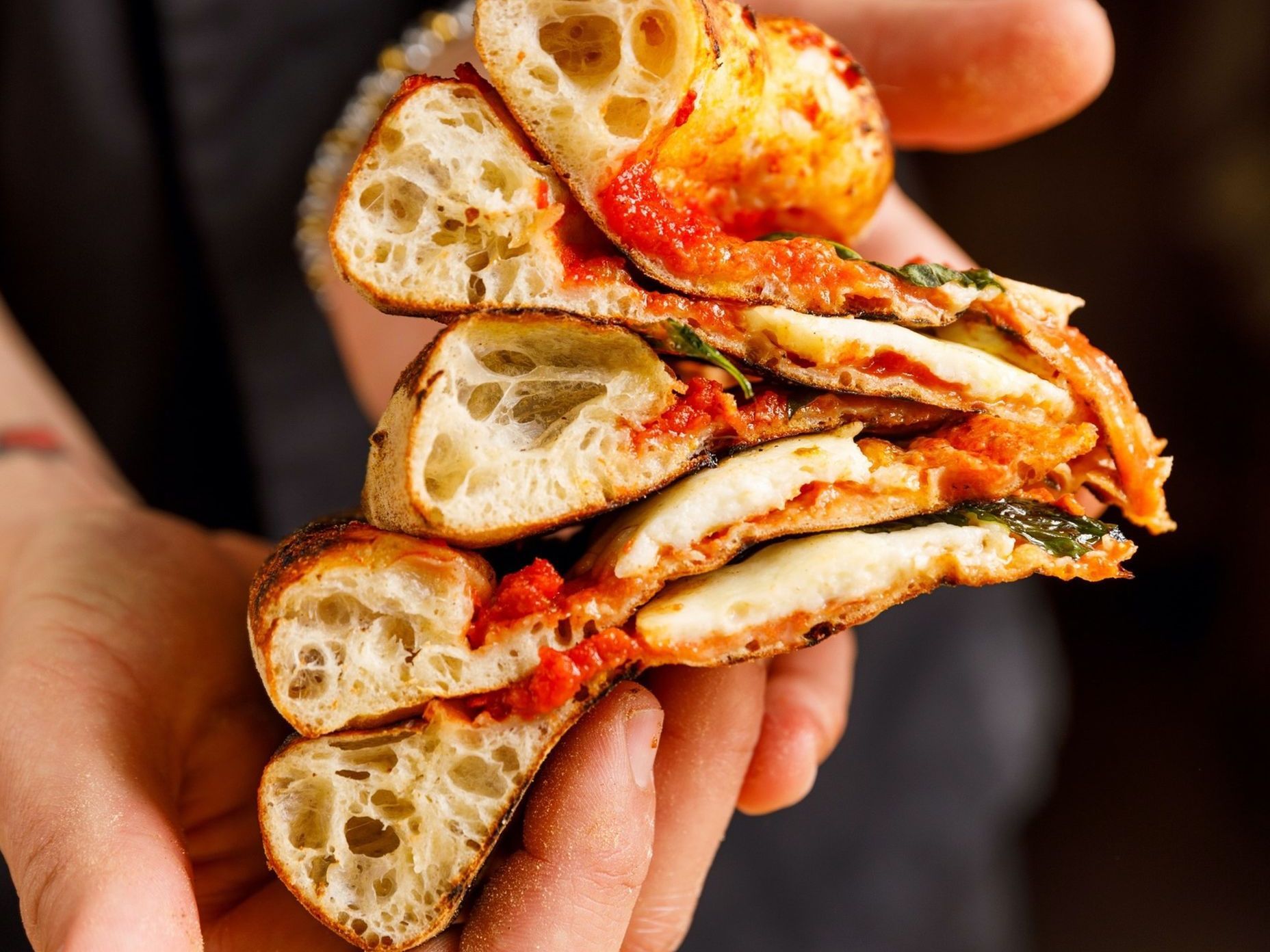 En person holder en sandwich med tomatsaus og ost i hendene.