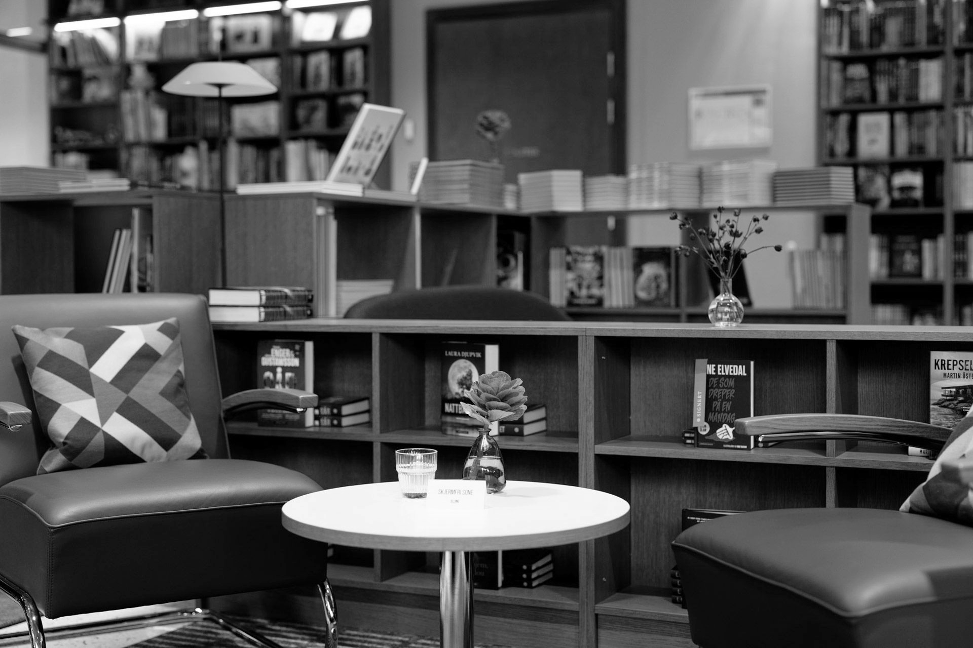 Svart-hvitt-bilde av en restaurantinteriør med bord, bar og rutete gulv.