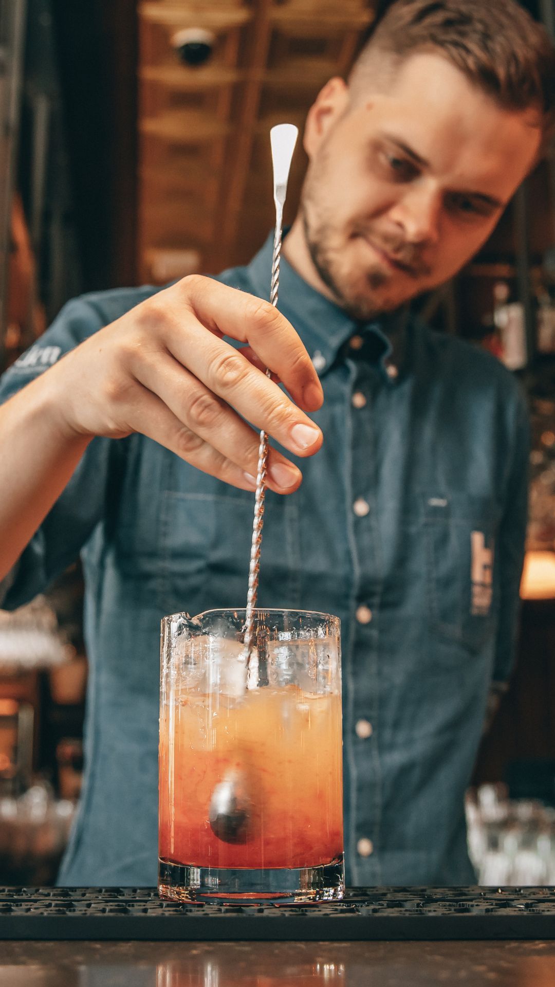 En bartender blander en drink med en skje i et glass.