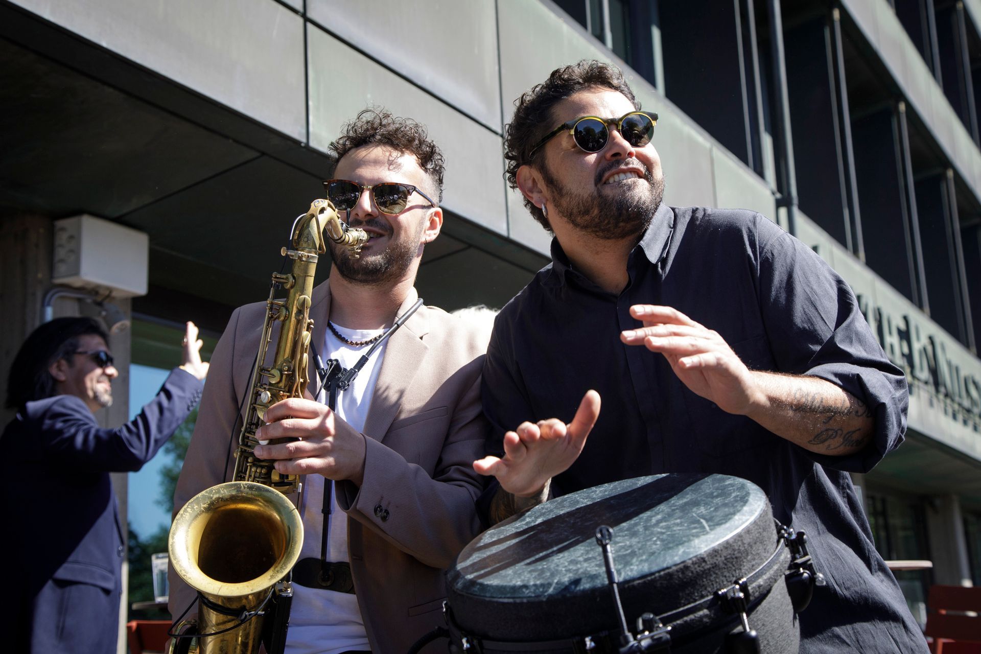 To menn spiller saksofon og tromme foran en bygning.