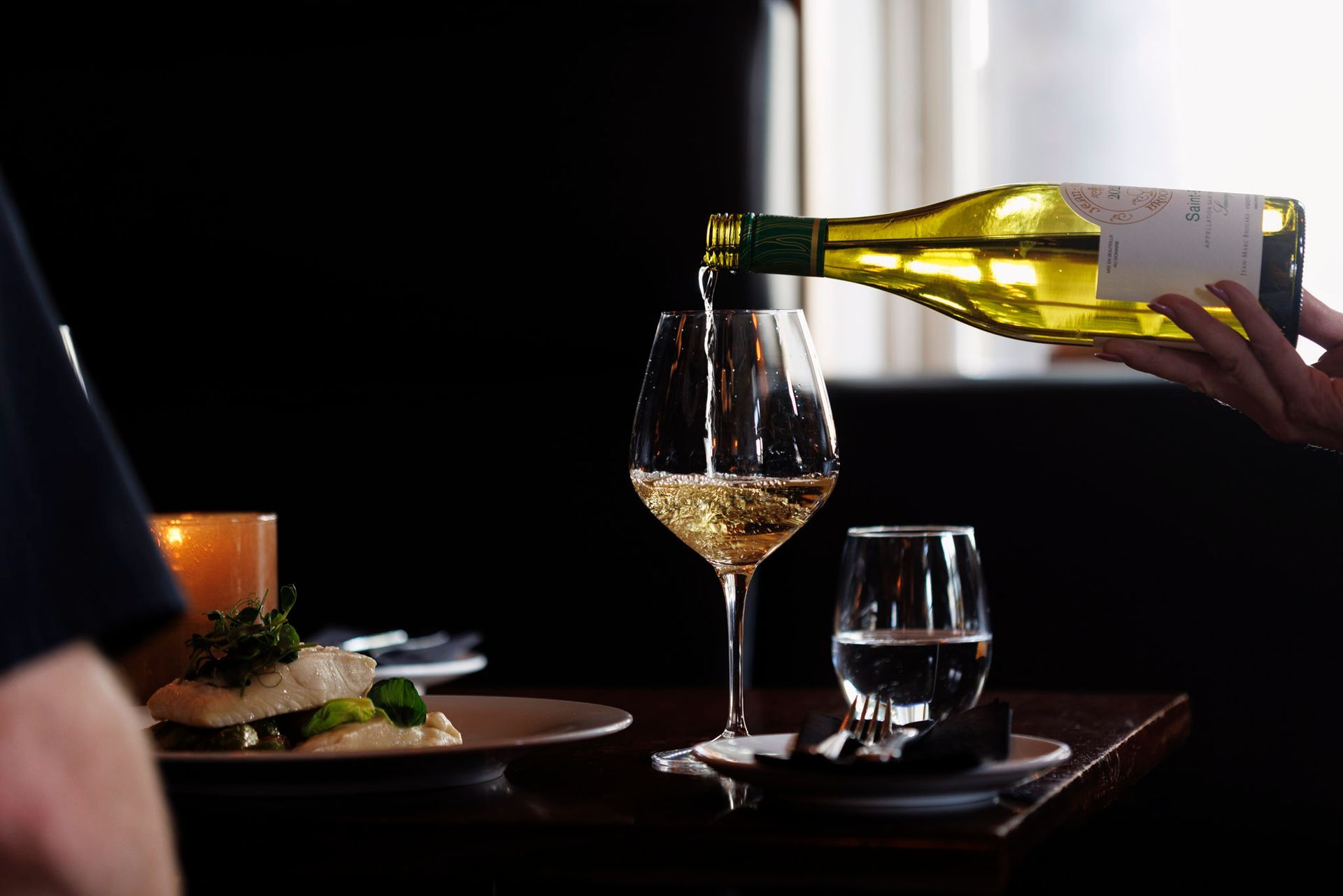 En person skjenker vin i et glass på et bord.