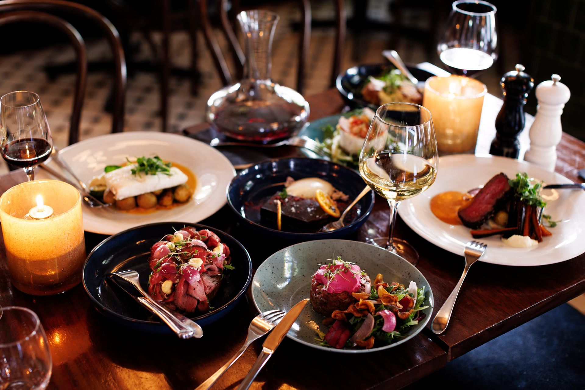 Et bord dekket med diverse tallerkener, vinglass og stearinlys i en restaurantsetting.