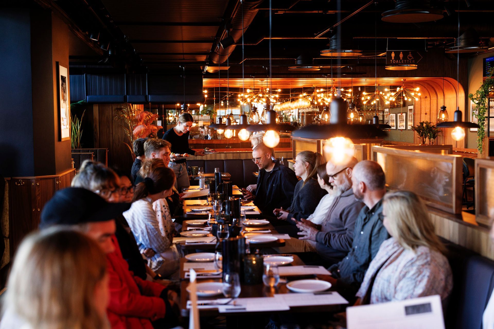 En gruppe mennesker sitter ved langbord på en restaurant.