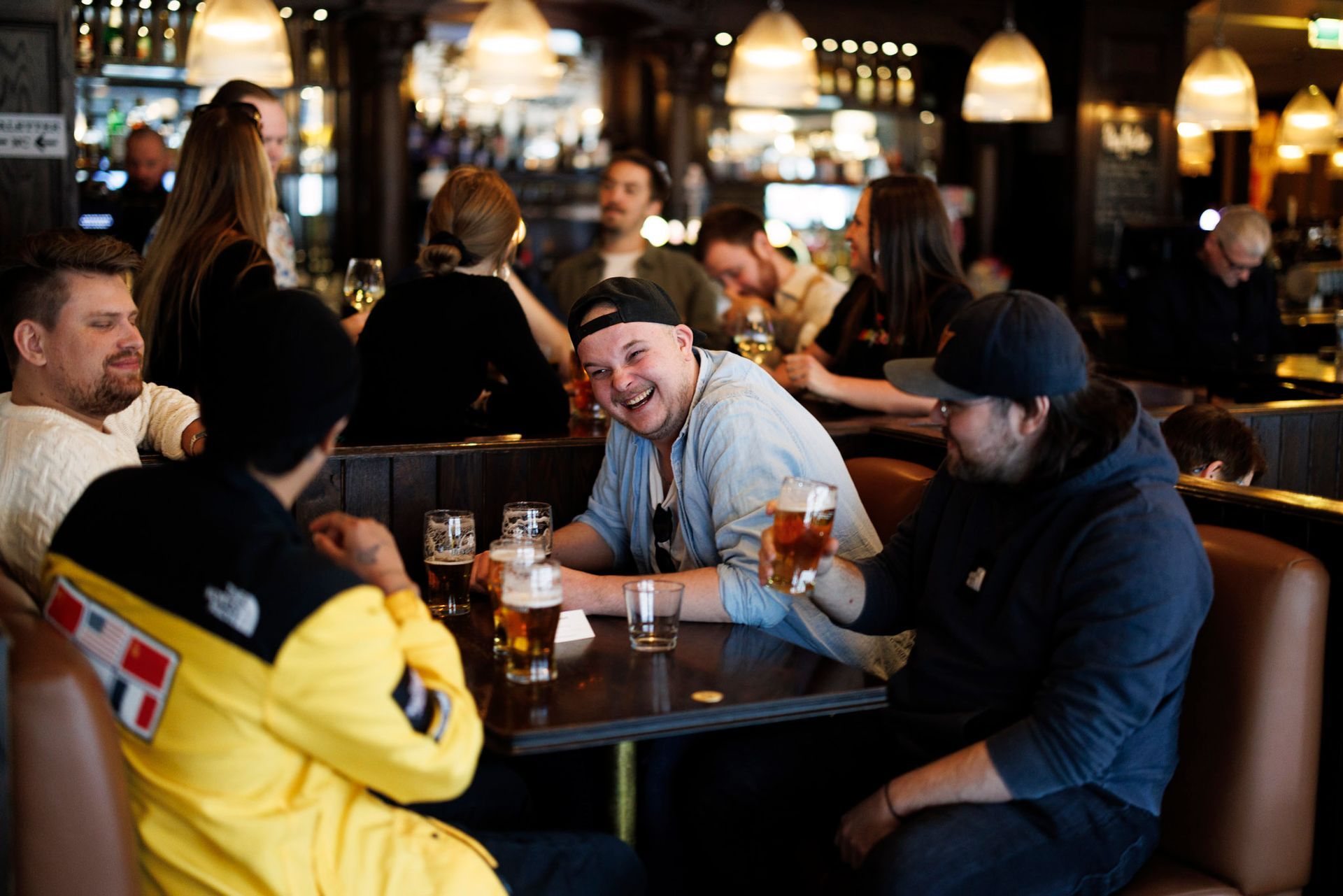 Folk samlet seg på en bar og drakk øl, noen smilte. Svakt opplyst interiør.