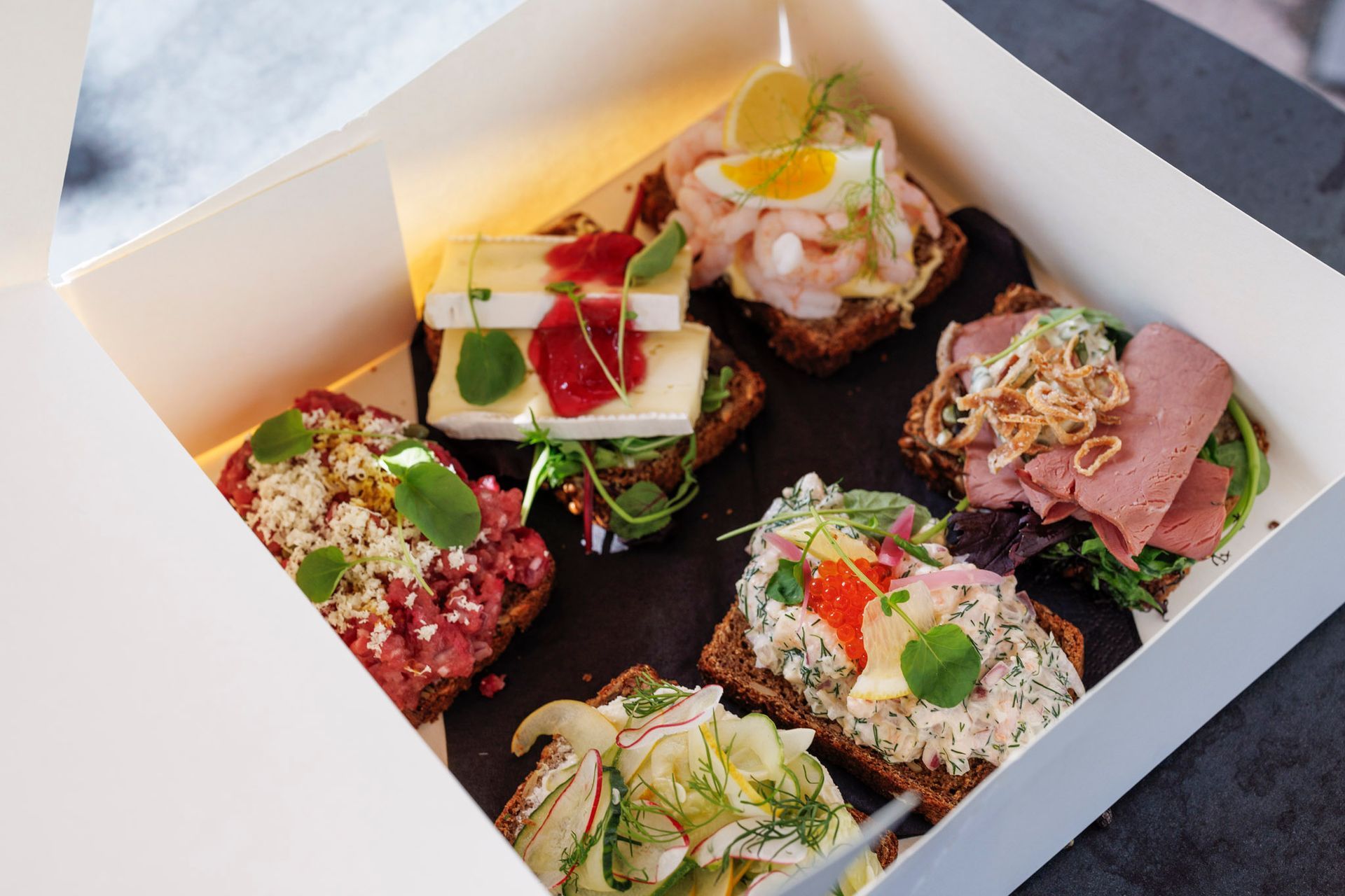 En boks fylt med en rekke smørbrød med forskjellige pålegg.