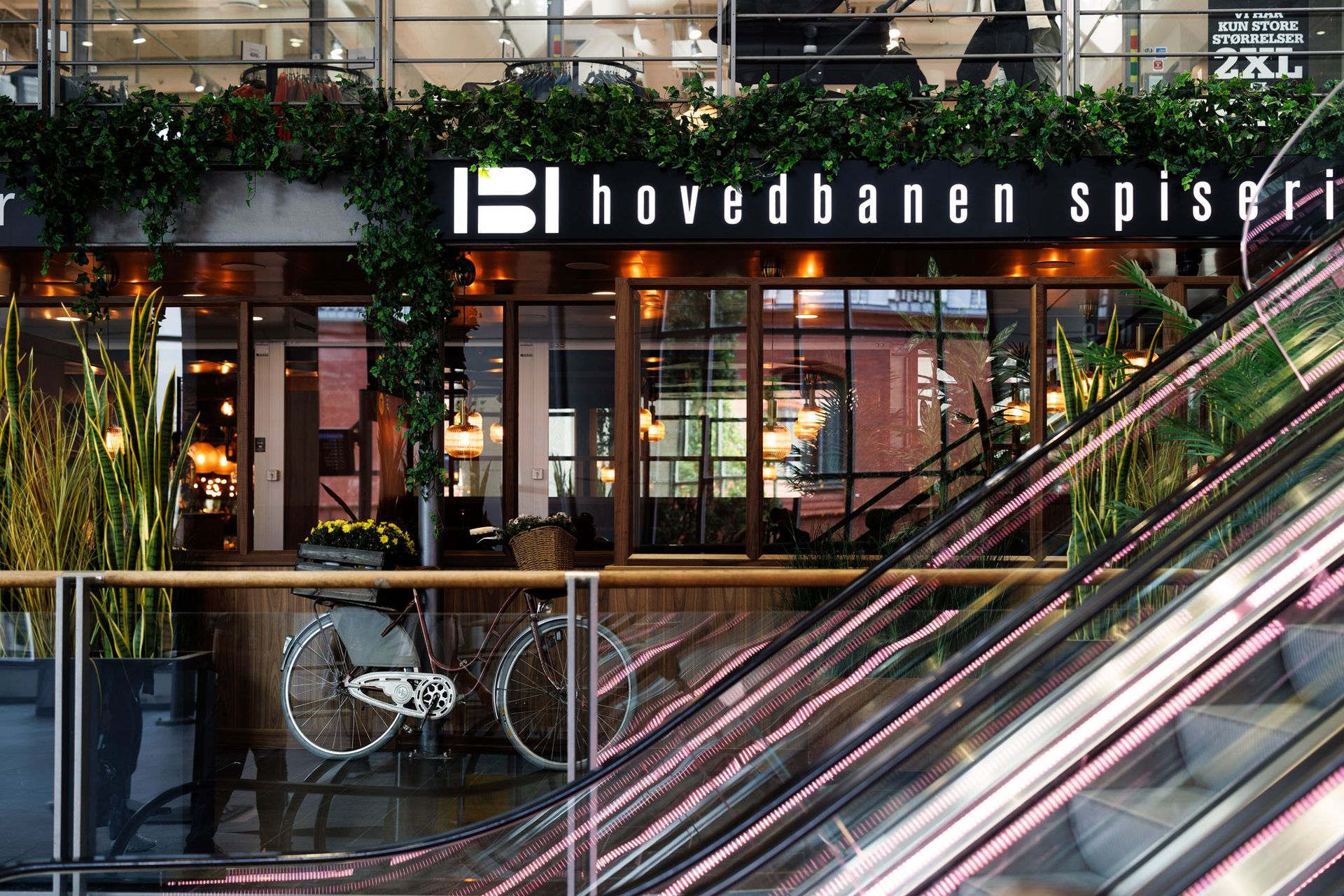 A bicycle is parked outside of a restaurant called hovedbanen spiseri