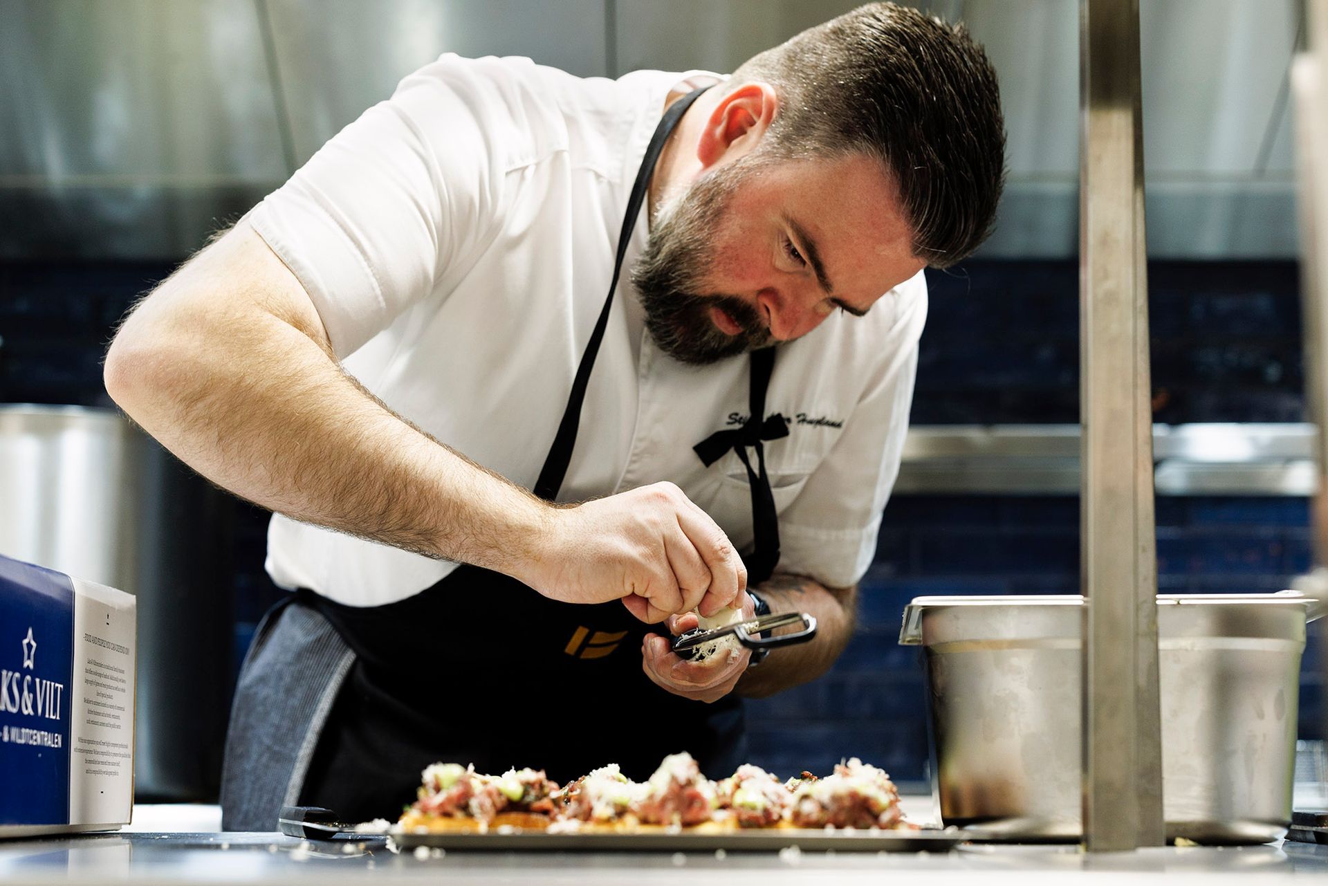 En mann i et forkle lager mat på et kjøkken.