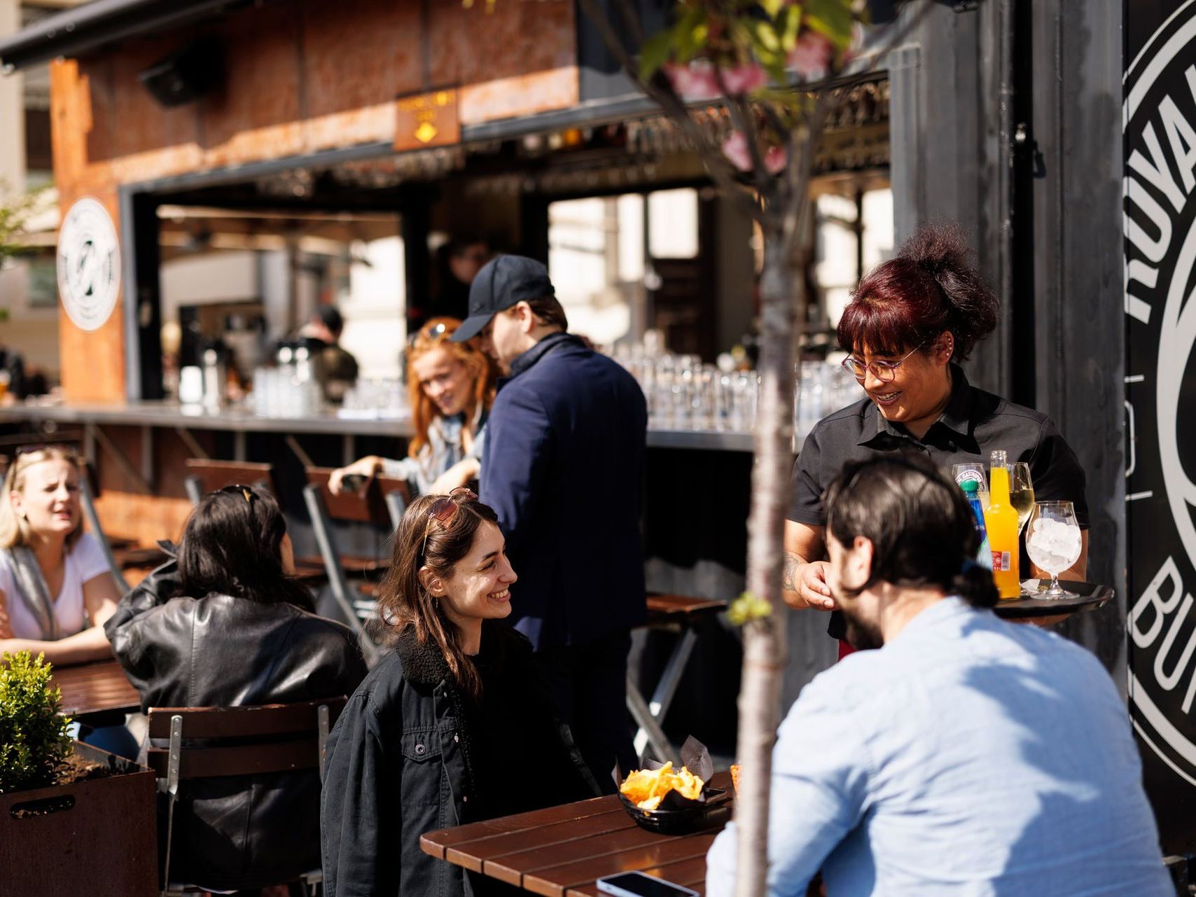 En gruppe mennesker sitter ved bordene utenfor en restaurant.