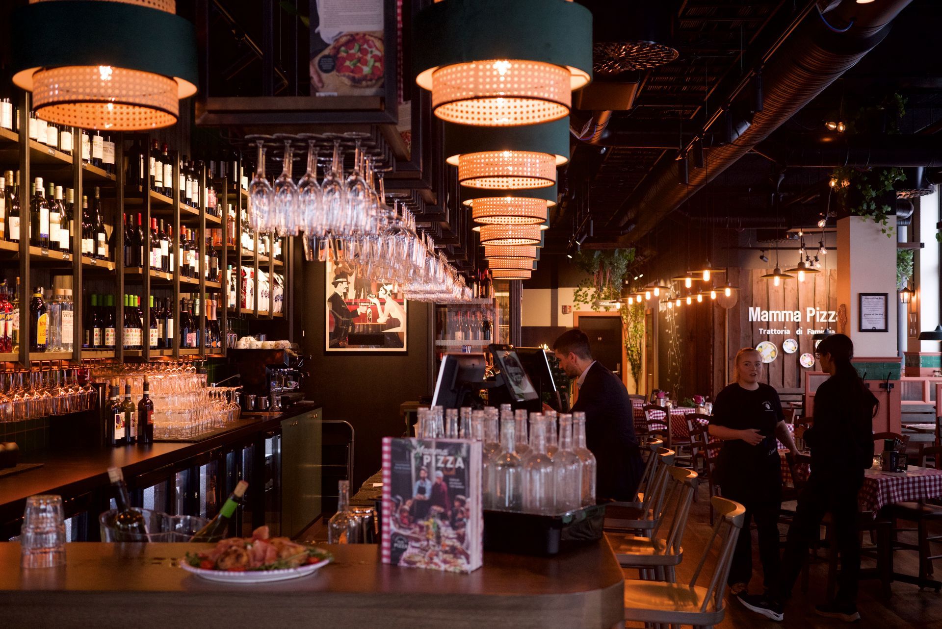 En restaurant med en lang bar og mange vinglass hengende i taket.