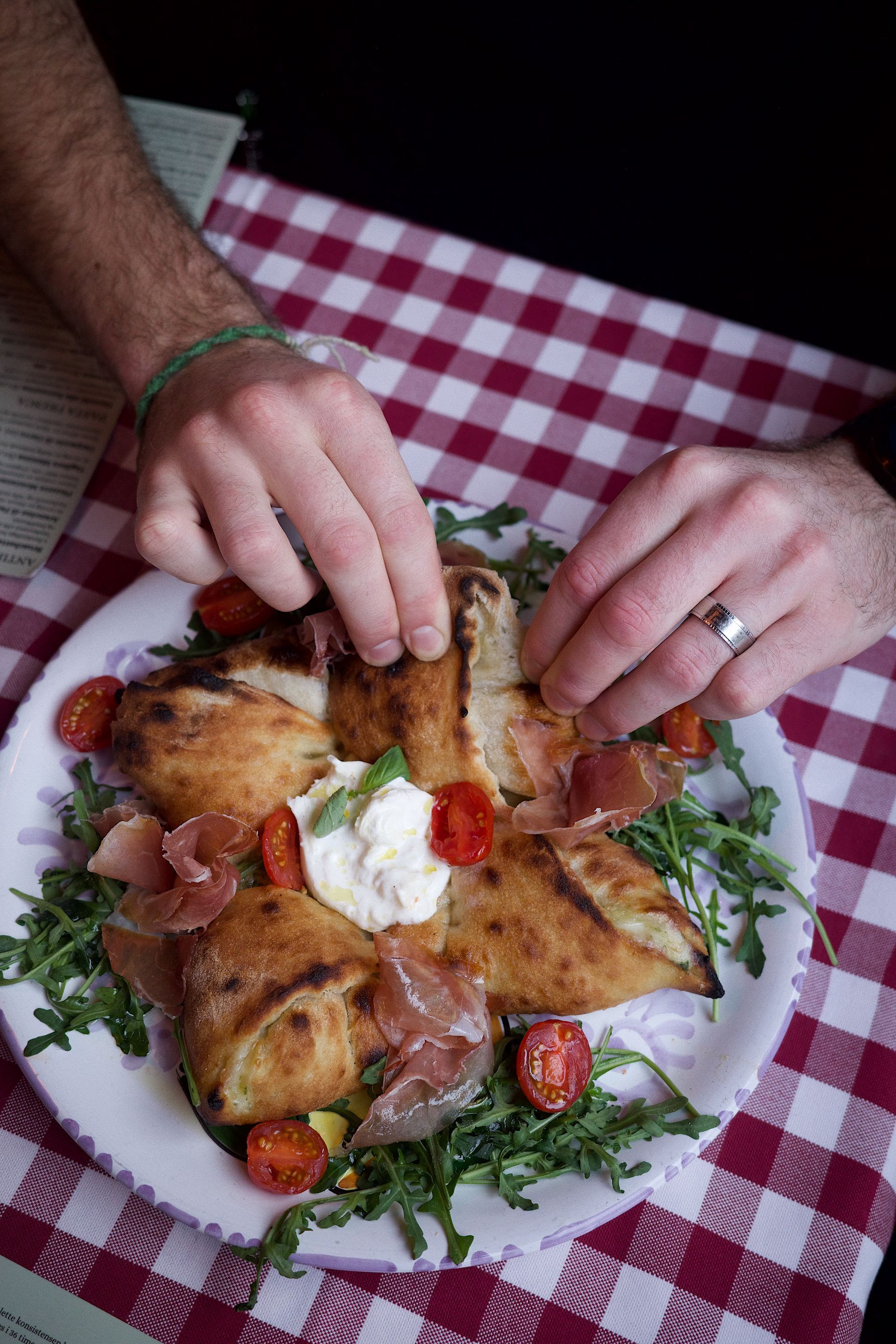 En person tar et stykke pizza fra en tallerken på et bord.