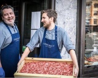 To menn med forkle holder en boks med reker.